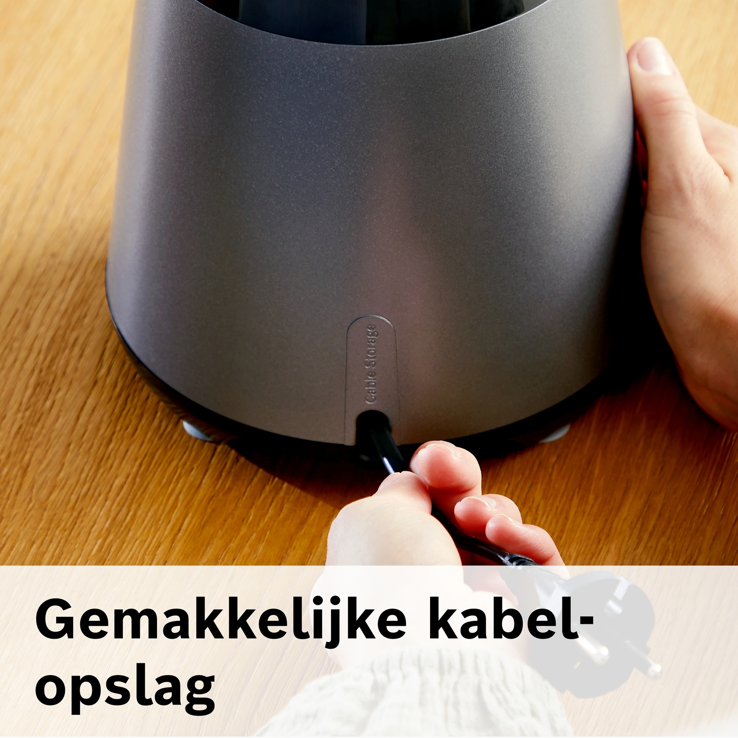 Person stows cable into a grey device on a wooden surface.