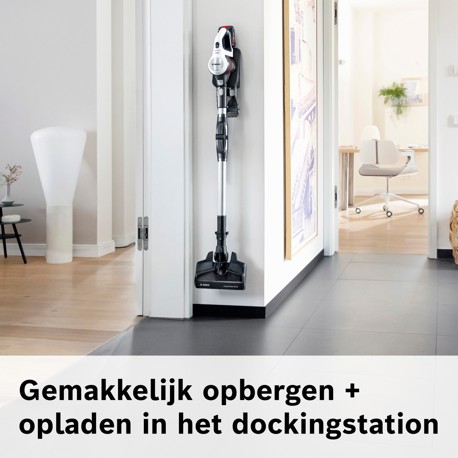 Een draadloze stofzuiger hangt aan een muurbeugel naast een deuropening.