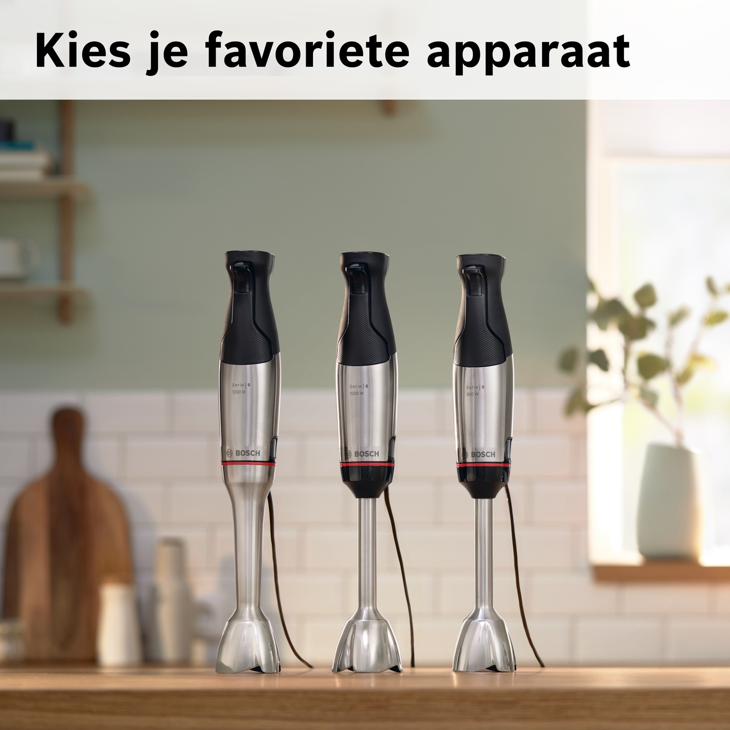 Drie zilveren staafmixers met zwarte handgrepen staan op een houten ondergrond.