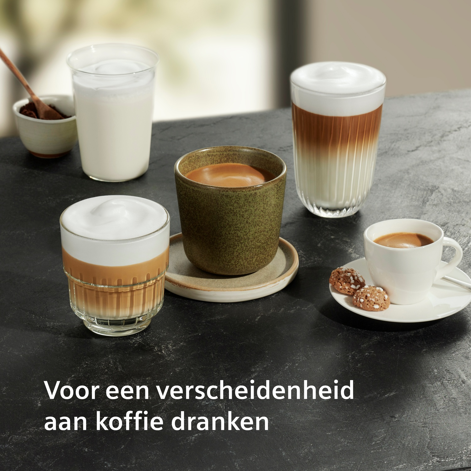 Diverse koffiedranken met melkschuim en koekjes op een tafel.