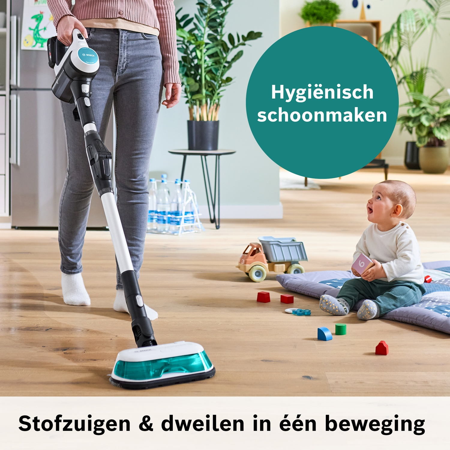Een persoon stofzuigt en dweilt de vloer terwijl een baby toekijkt.