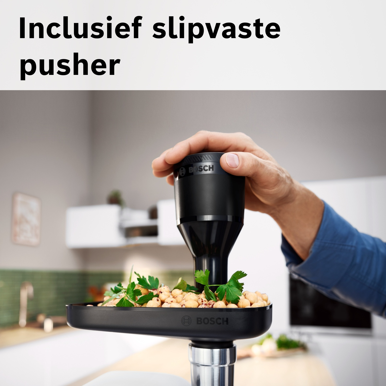 Een hand houdt een zwarte pusher vast boven een kom met kikkererwten en peterselie.