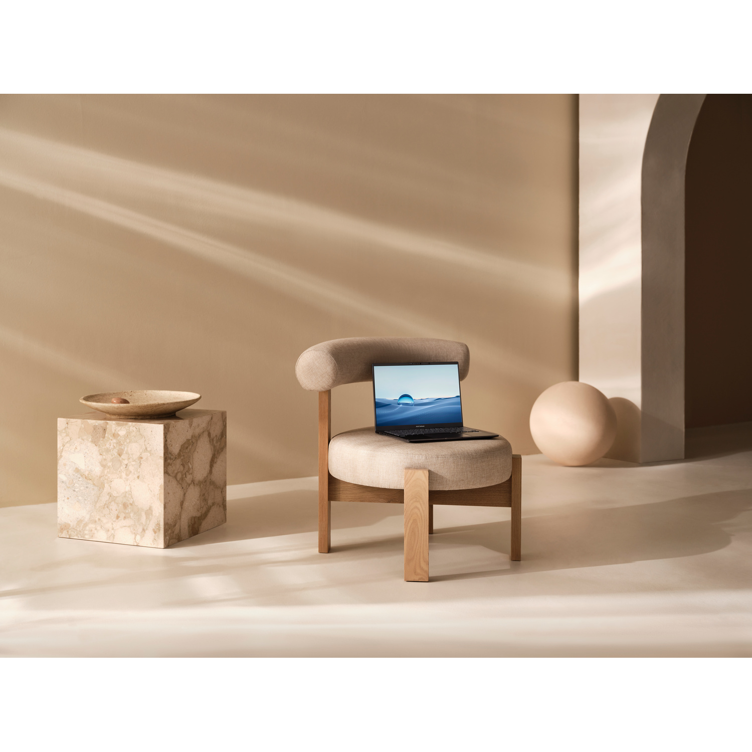 Un laptop poggia su una sedia imbottita accanto a un cubo di marmo con una ciotola. Una sfera sullo sfondo.