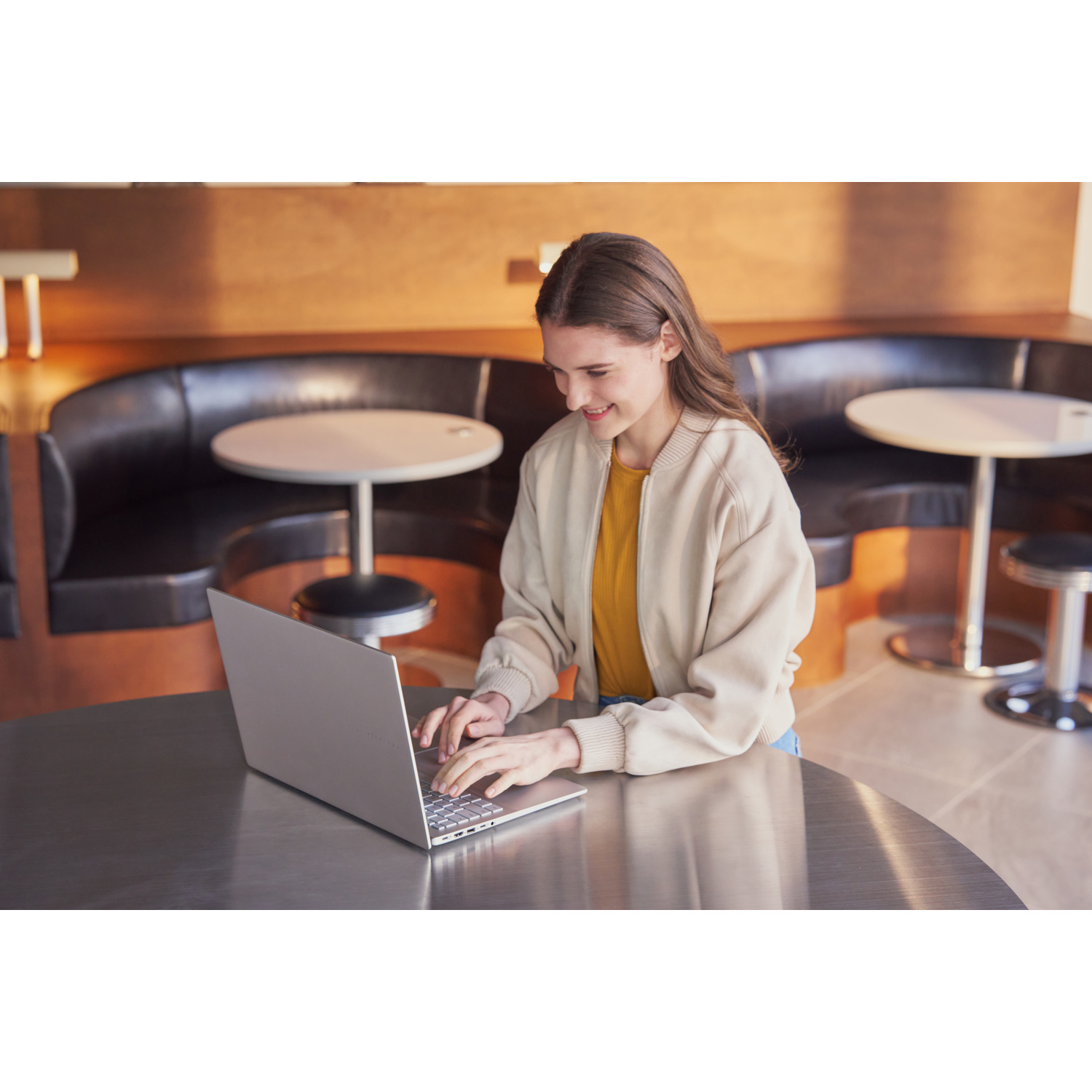Giovane donna digita su laptop in caffè moderno con tavoli rotondi.