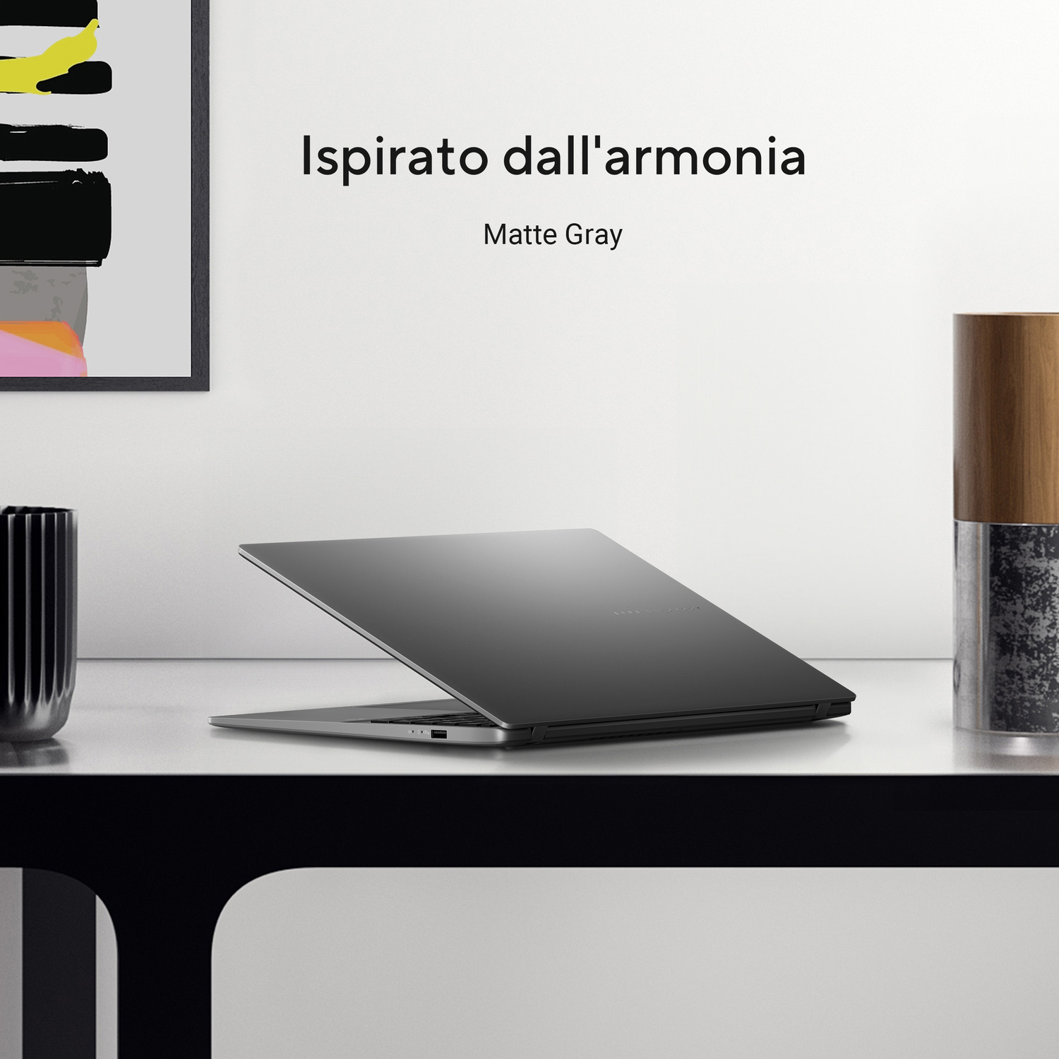 Un laptop grigio opaco è aperto su una scrivania bianca. Il testo dice 'Ispirato dall'armonia'.