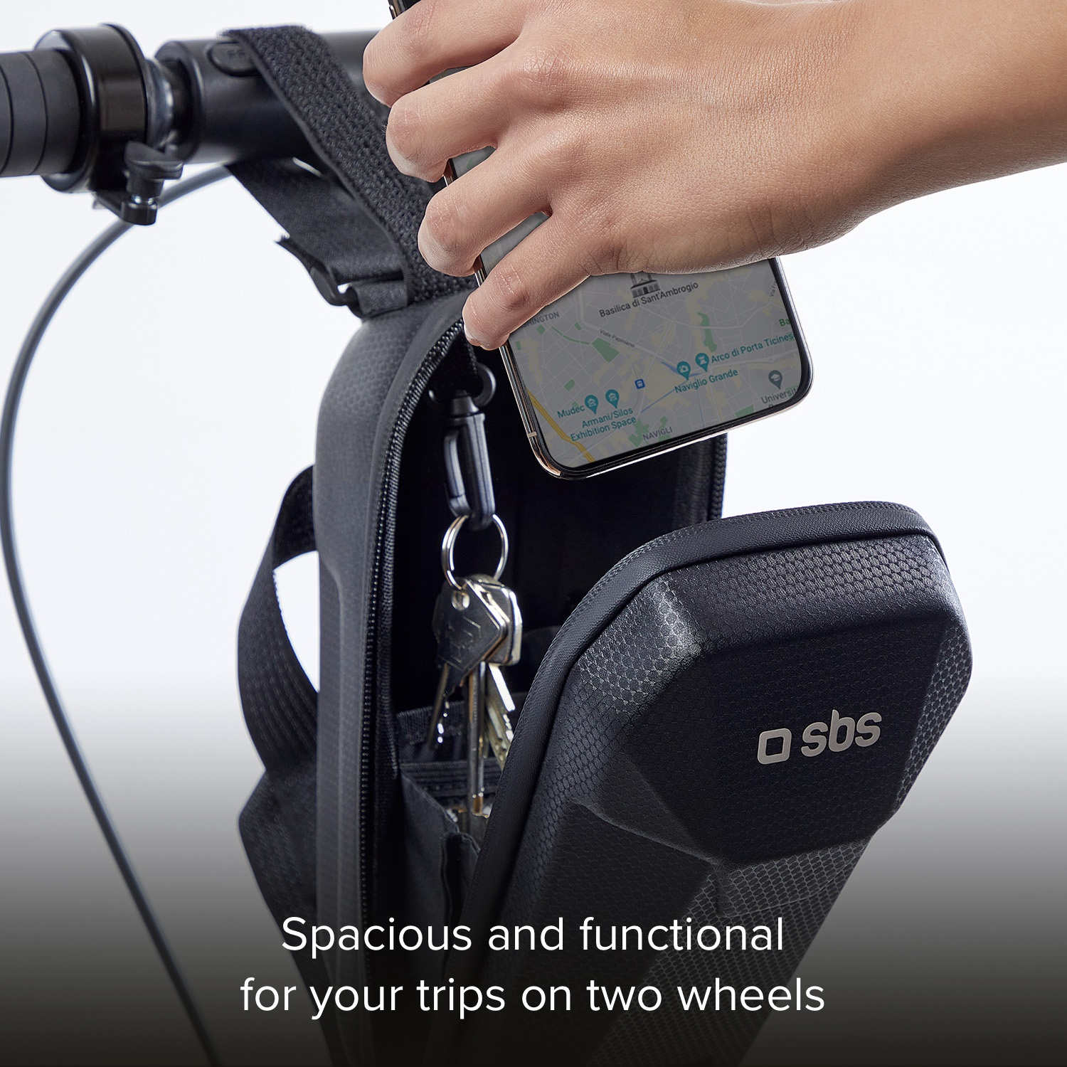 A hand holds a phone over a black bike bag containing keys.
