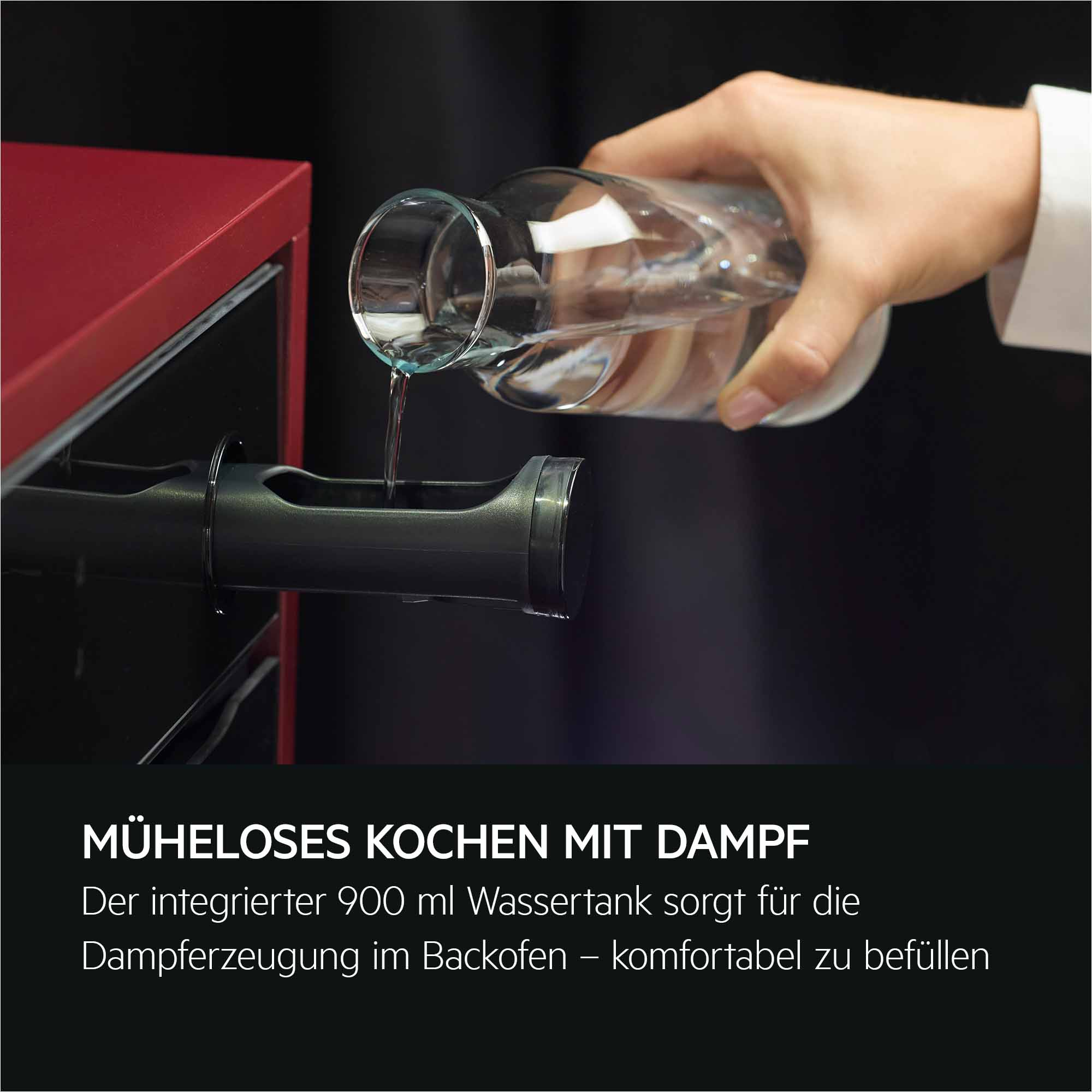 Eine Hand füllt Wasser aus einem Glasbehälter in einen Backofen-Wassertank.