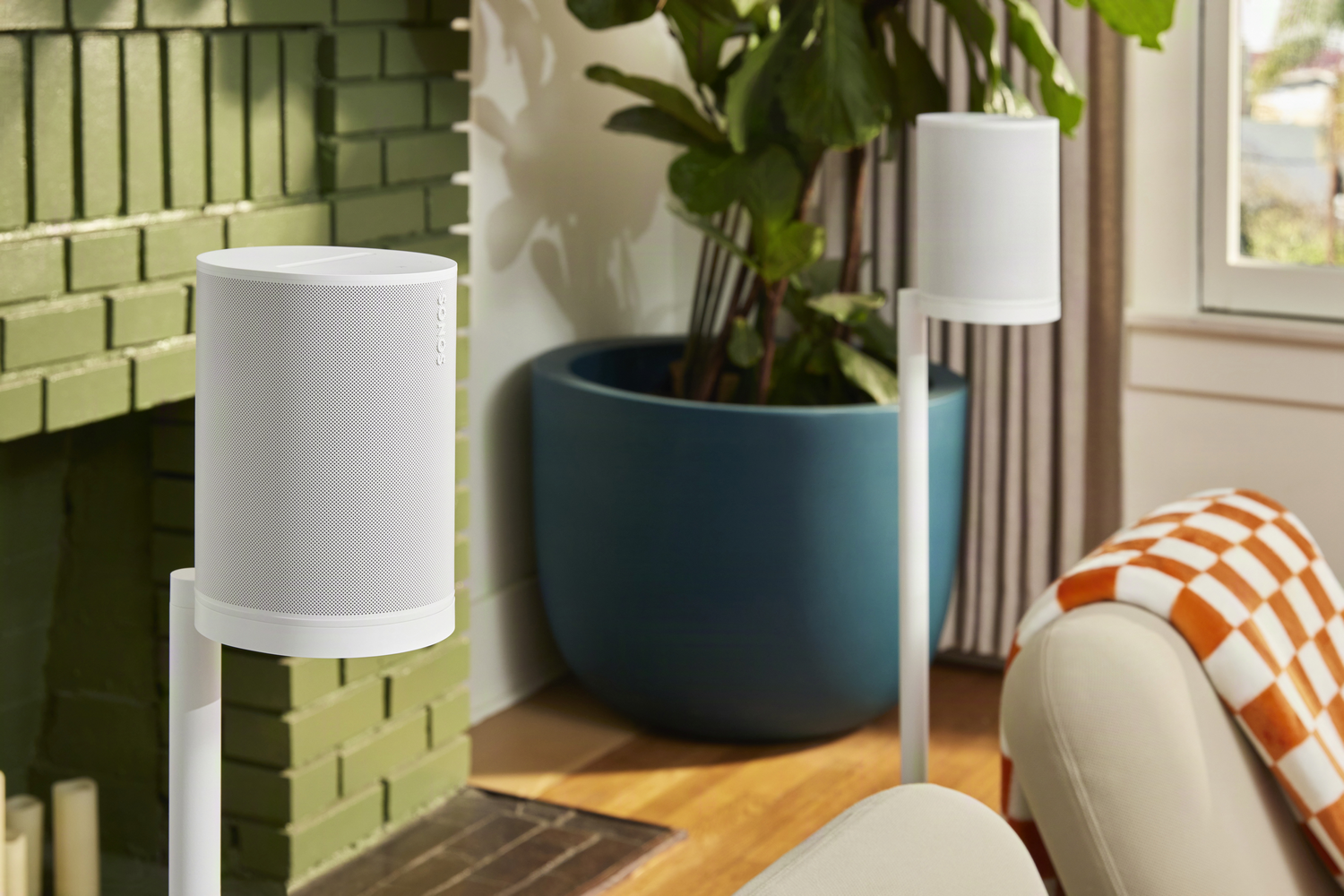 Altavoces blancos junto a una chimenea de ladrillo verde y una maceta azul grande.