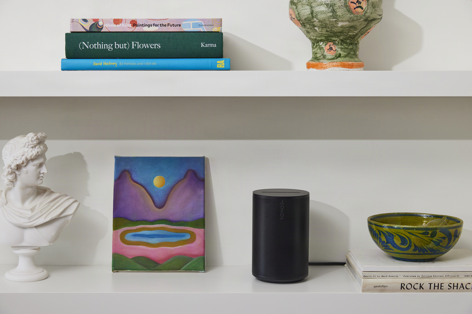 Estantes con libros, busto, pintura, altavoz y cuenco decorativo.