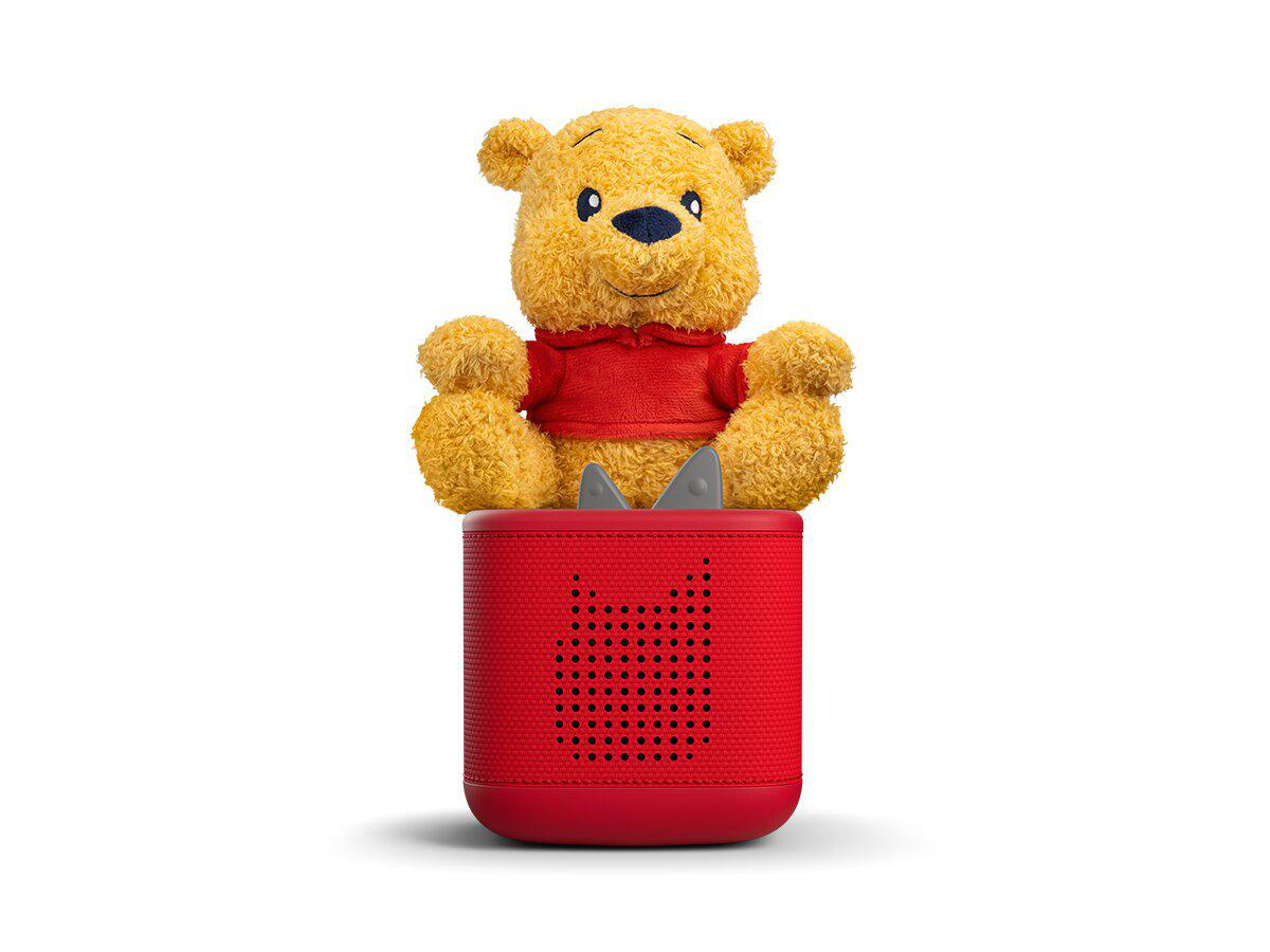 Ein flauschiger Winnie Puuh Bär in rotem Hemd sitzt auf einem roten Lautsprecher.