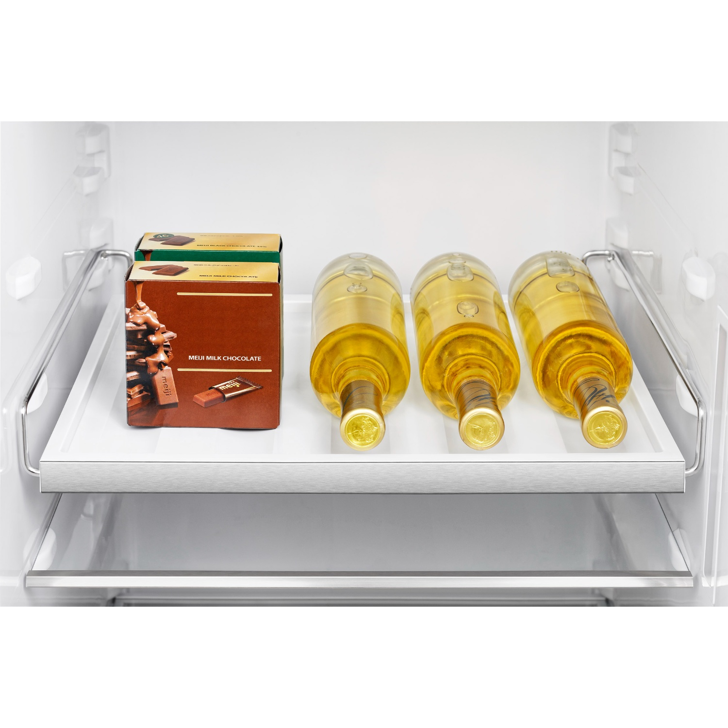 Three bottles of wine and two boxes of chocolate on a white tray in a refrigerator.
