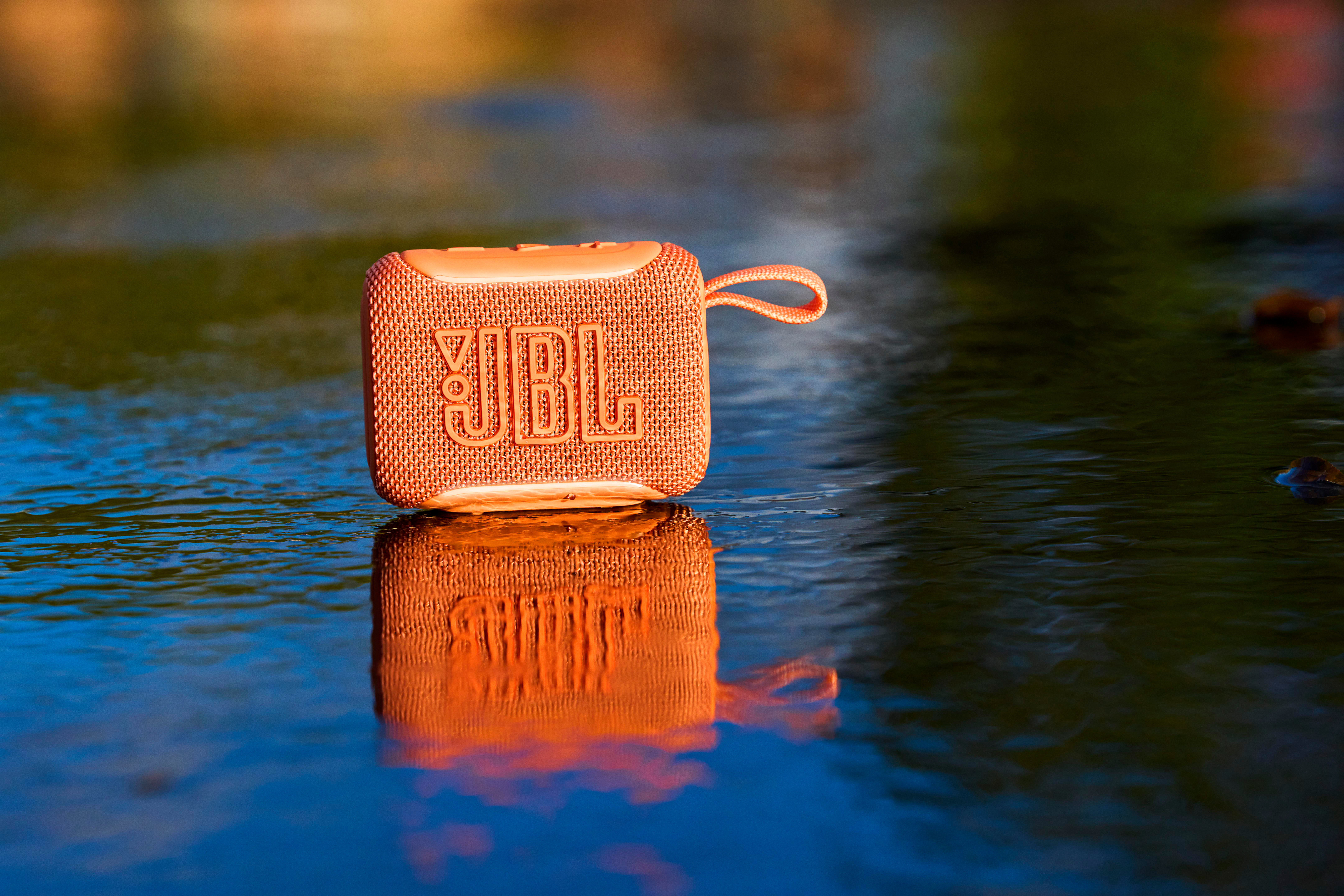 Eine orange JBL-Lautsprecherbox steht im Wasser, mit Reflexion.