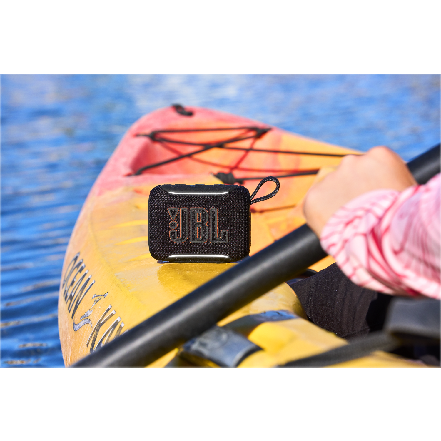 A black JBL speaker rests on a yellow kayak floating on blue water.