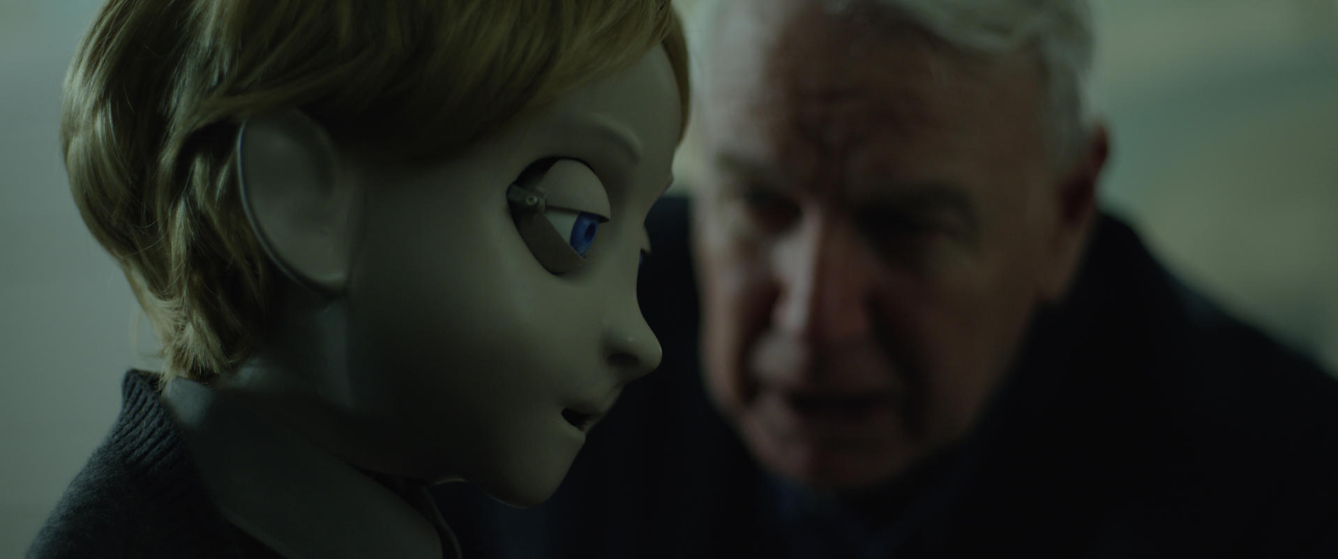 Ein Mann spricht mit einer Puppe mit blauen Augen und blonden Haaren.