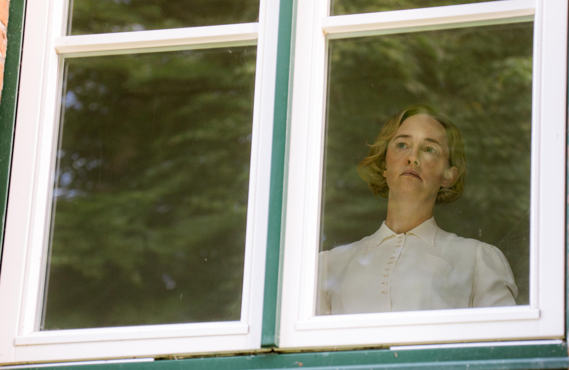 Eine Frau mit blondem Haar blickt durch ein Fenster nach draußen.