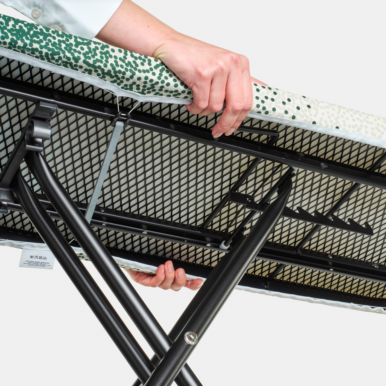 Person holding an ironing board with a green polka dot pattern and metal frame.