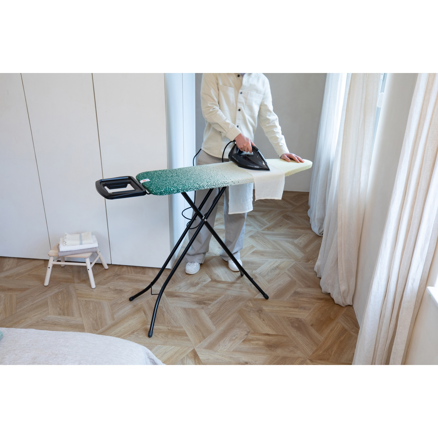 Person ironing a white cloth on a green patterned ironing board.