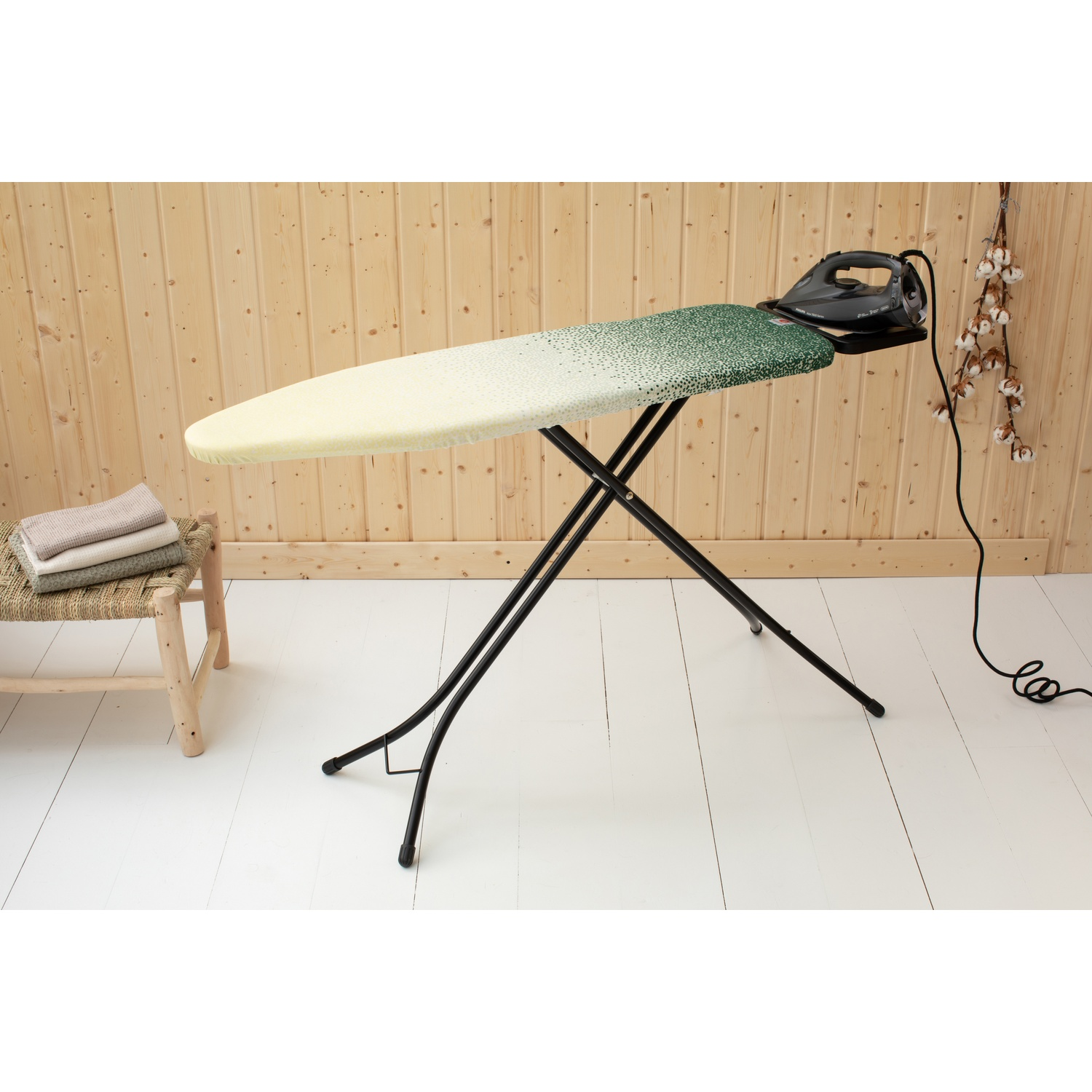 Iron on an ironing board with a green and yellow cover, next to towels.