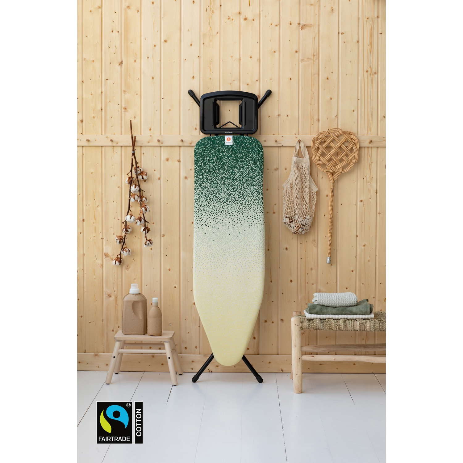 An ironing board with a green-yellow pattern stands against a wooden wall.