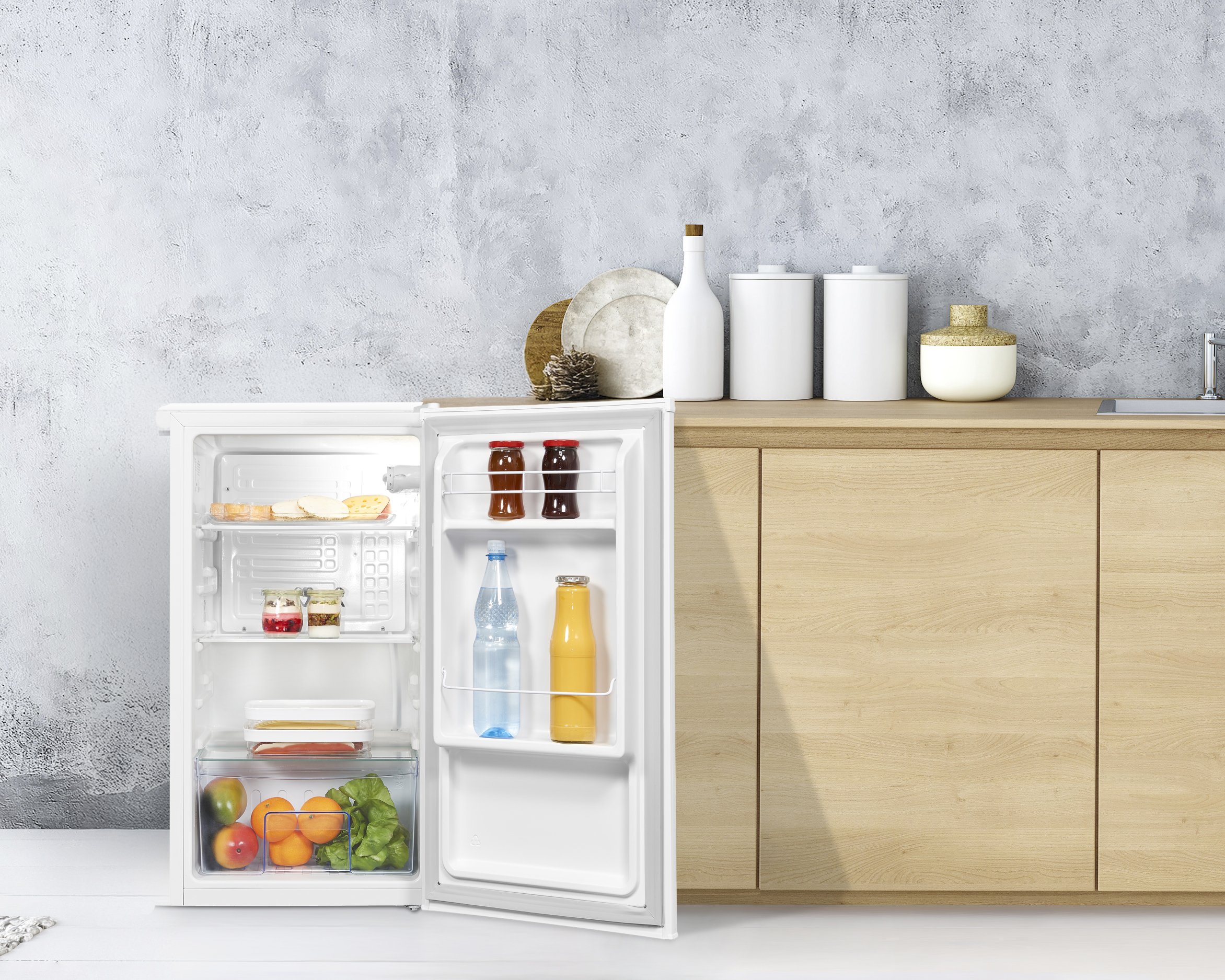 Ein offener weißer Kühlschrank mit Lebensmitteln, daneben Holzschränke.