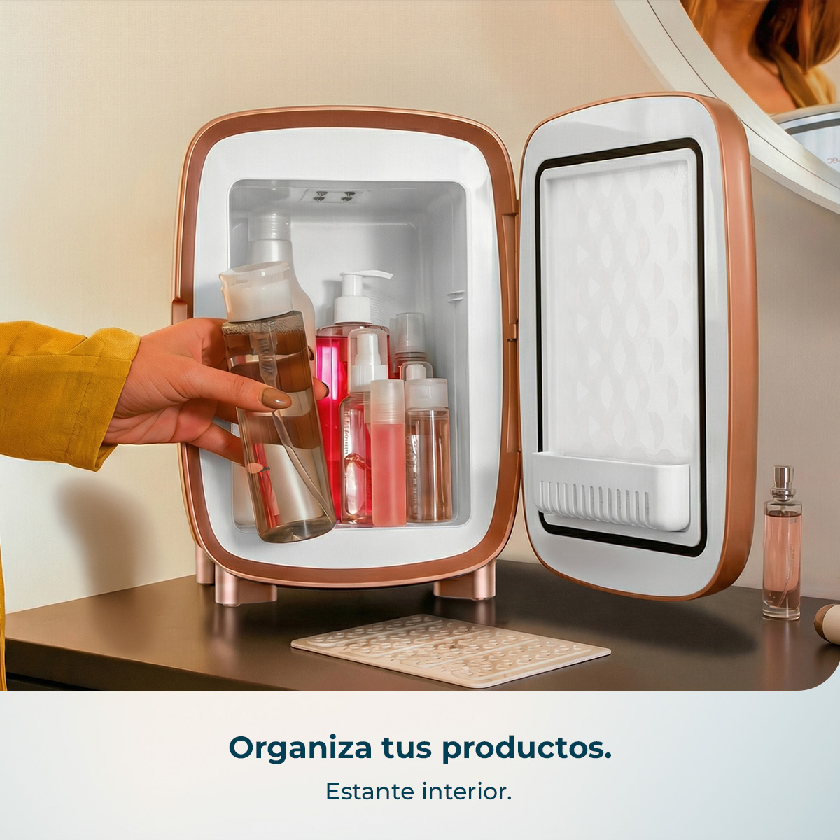 Una mano saca una botella transparente de un mininevera abierto color oro rosa con cosméticos.