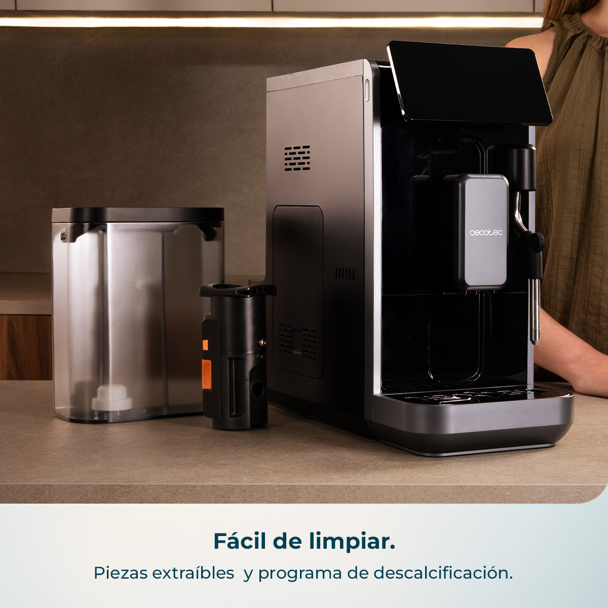 Moderna cafetera con depósito de agua y herramienta de limpieza en encimera.