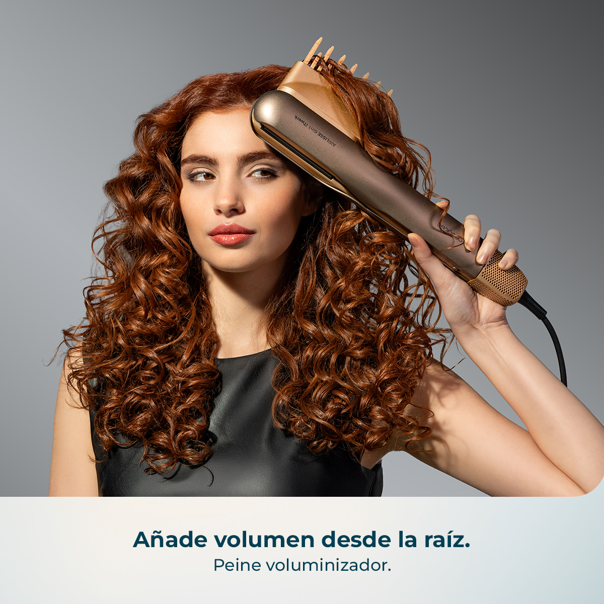 Mujer con pelo rizado rojo se peina con un rizador dorado sobre fondo gris.