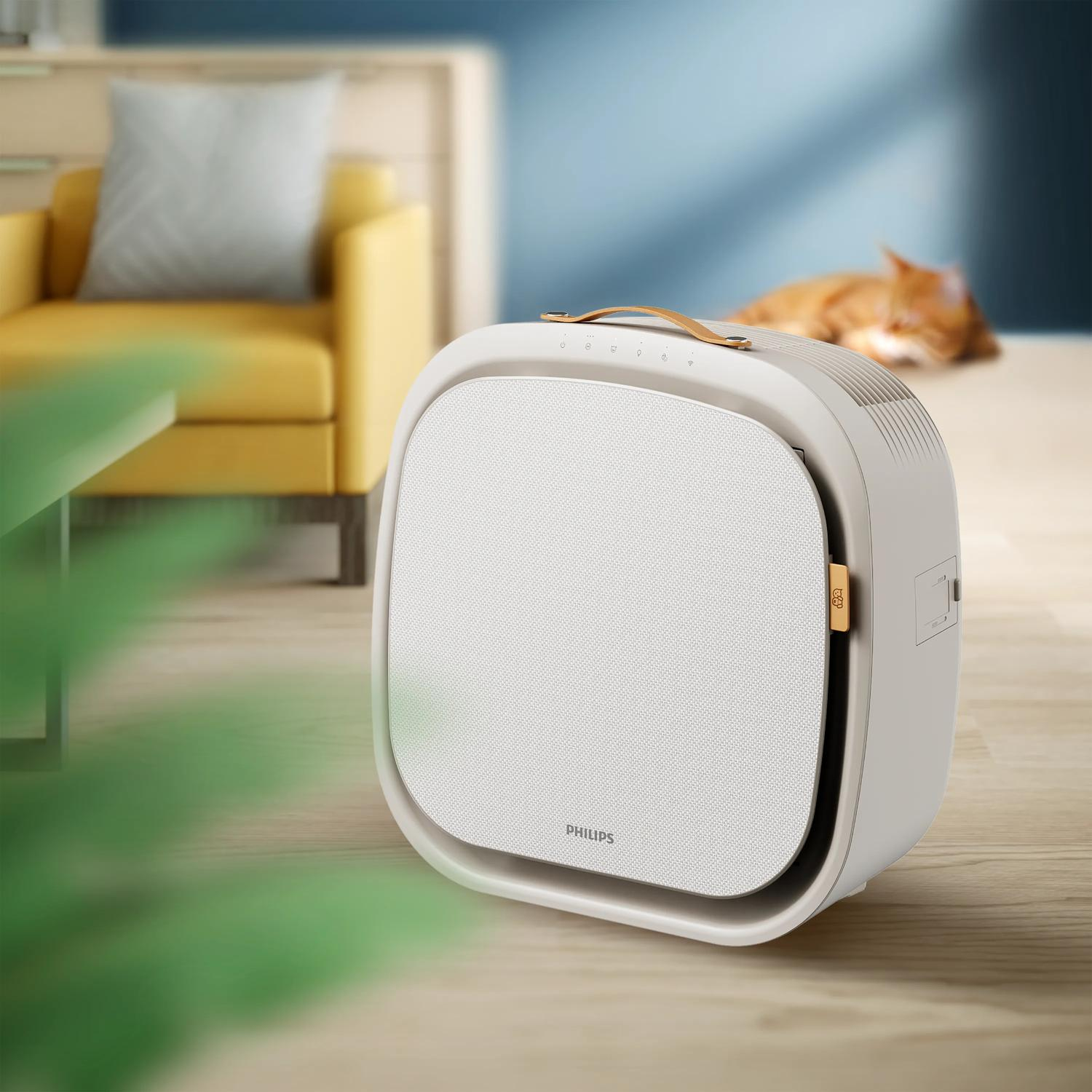 Un purificateur d'air Philips blanc sur un plancher en bois. Un fauteuil jaune et un chat flous en arrière-plan.