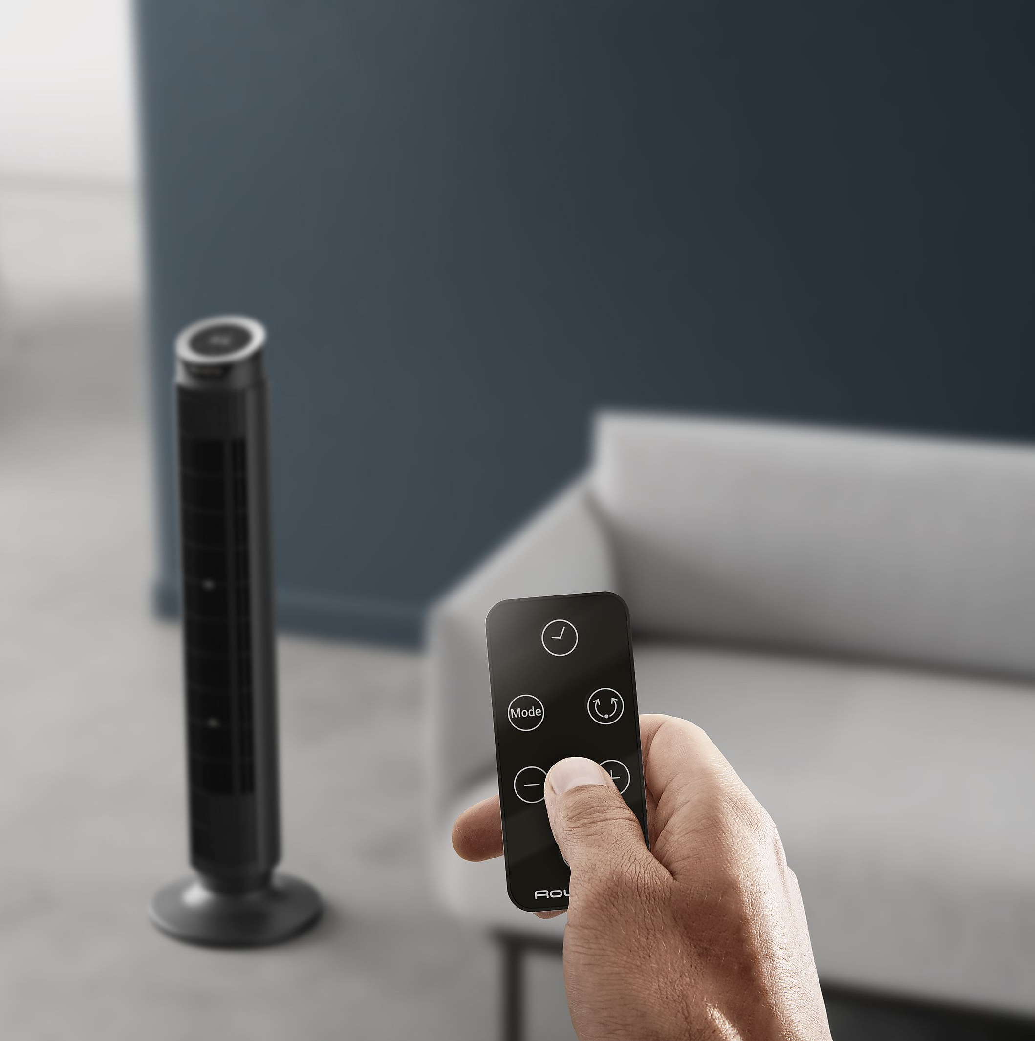 Una mano tiene un telecomando davanti a un ventilatore nero sottile.