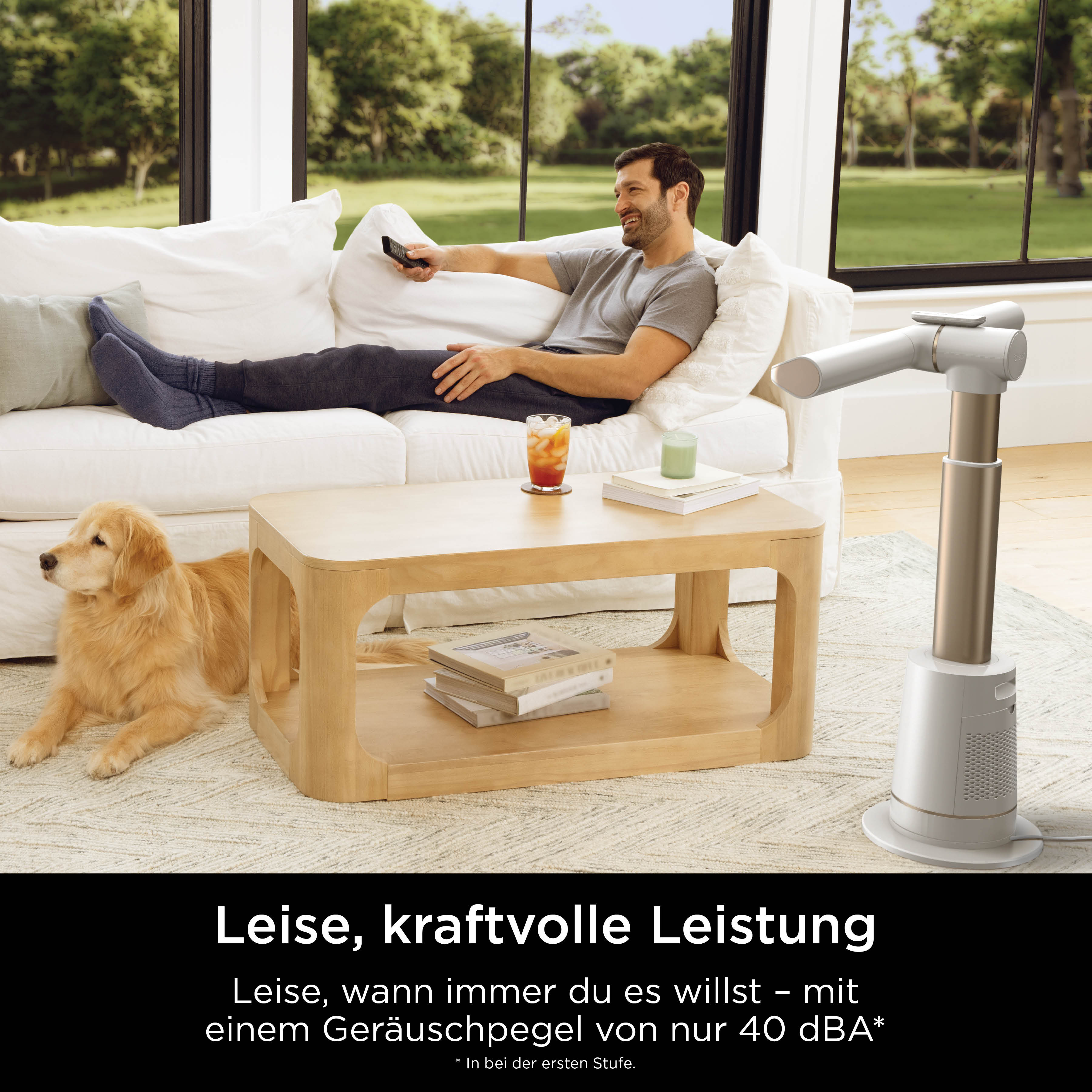 Mann entspannt auf Sofa mit Hund, ein Ventilator steht daneben.