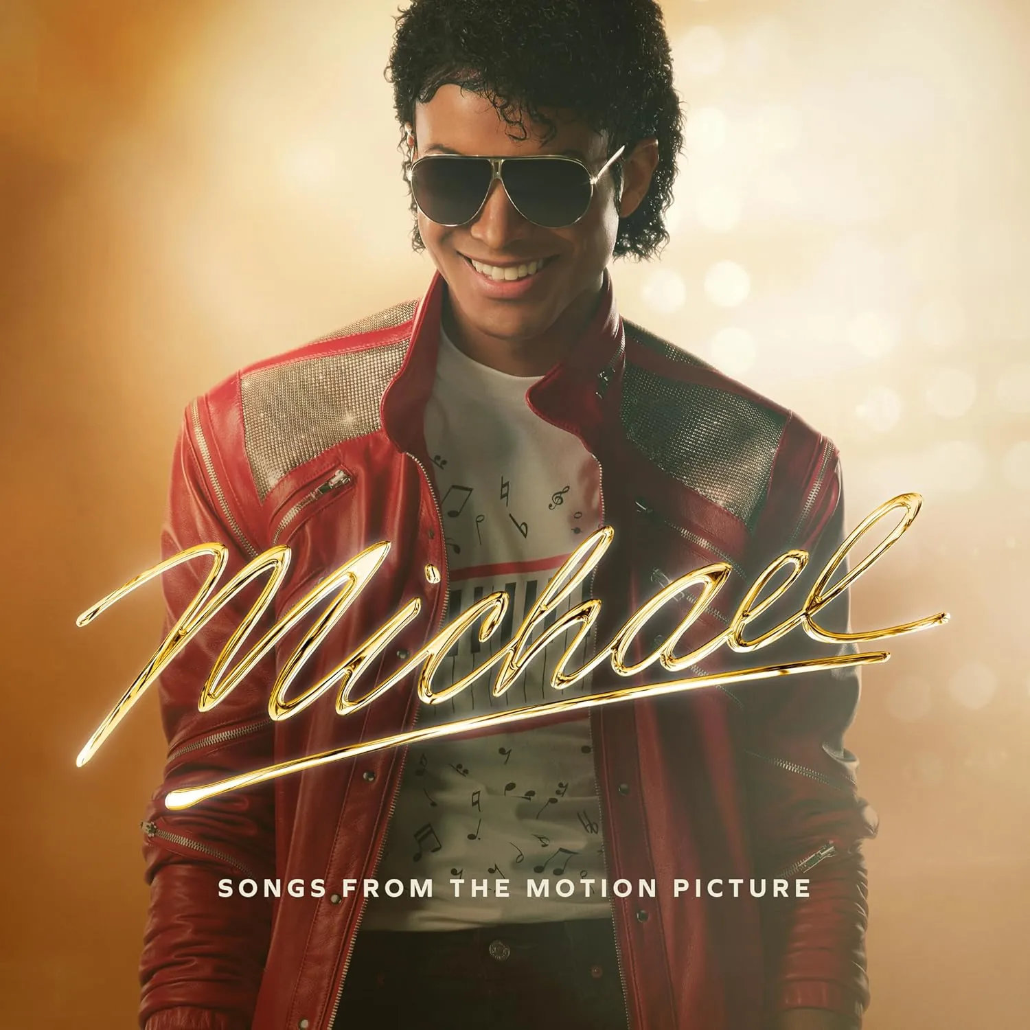 A man in a red leather jacket wearing sunglasses smiles, with golden light behind him.