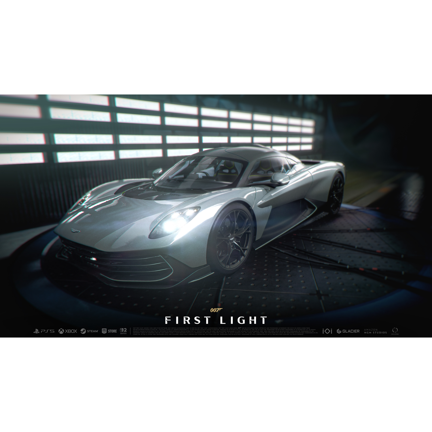 A silver Aston Martin with illuminated headlights sits in a dark garage.