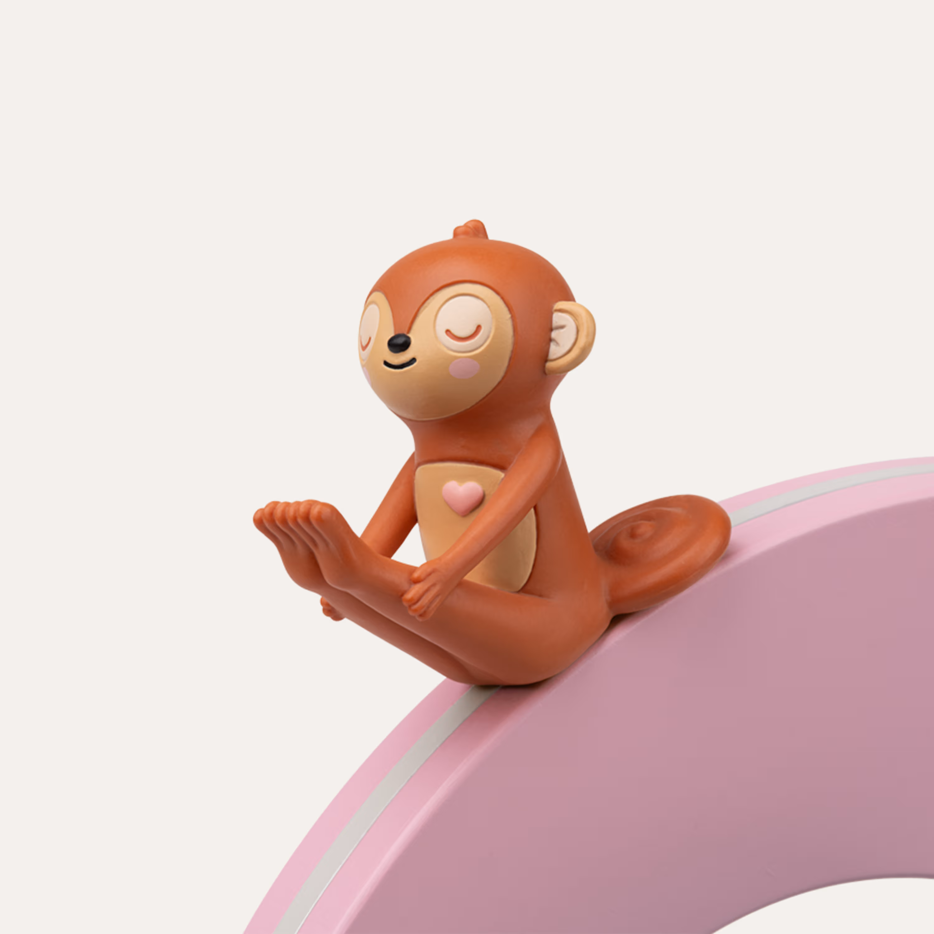 Eine braune Affenfigur sitzt mit geschlossenen Augen auf einem rosa Bogen.