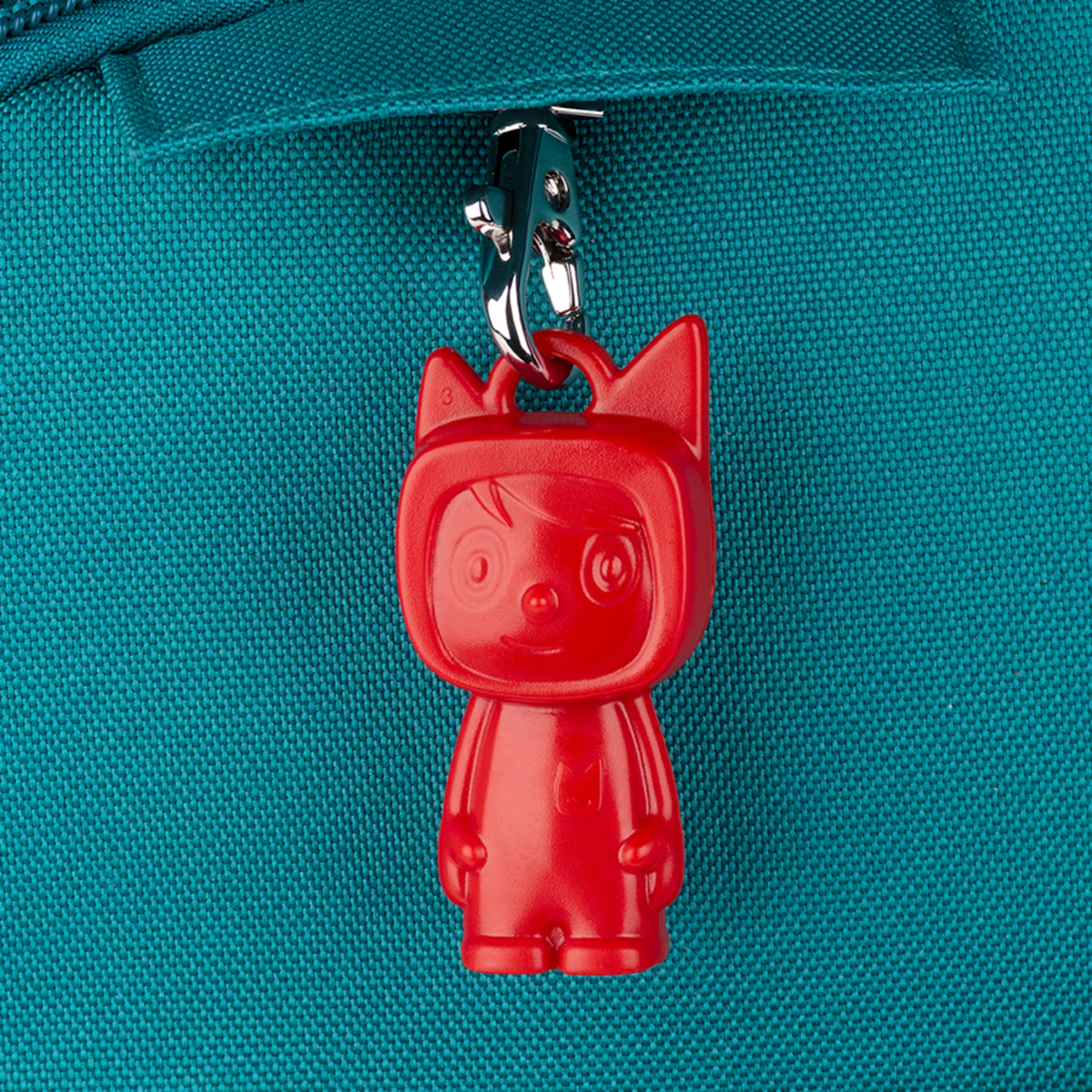Un ciondolo a forma di gatto rosso attaccato alla cerniera di una borsa turchese.