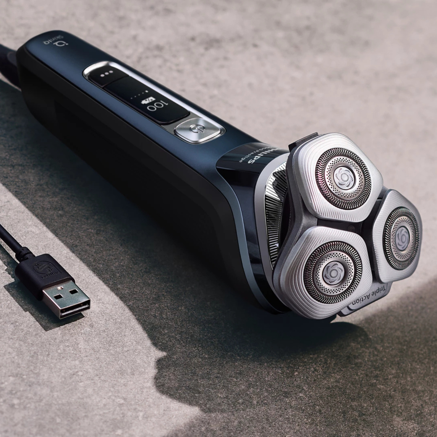 Una afeitadora eléctrica negra con tres cabezales giratorios y cable de carga USB.