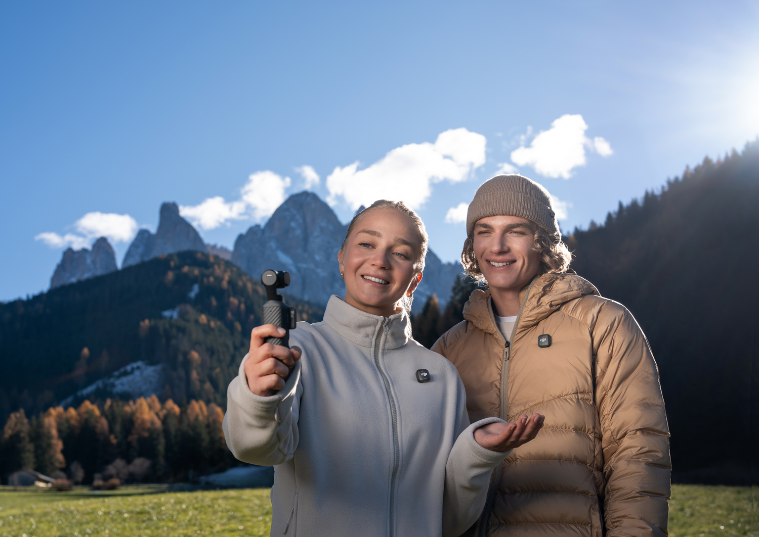 Hombre y mujer frente a montañas, mujer sostiene cámara, sonriendo.