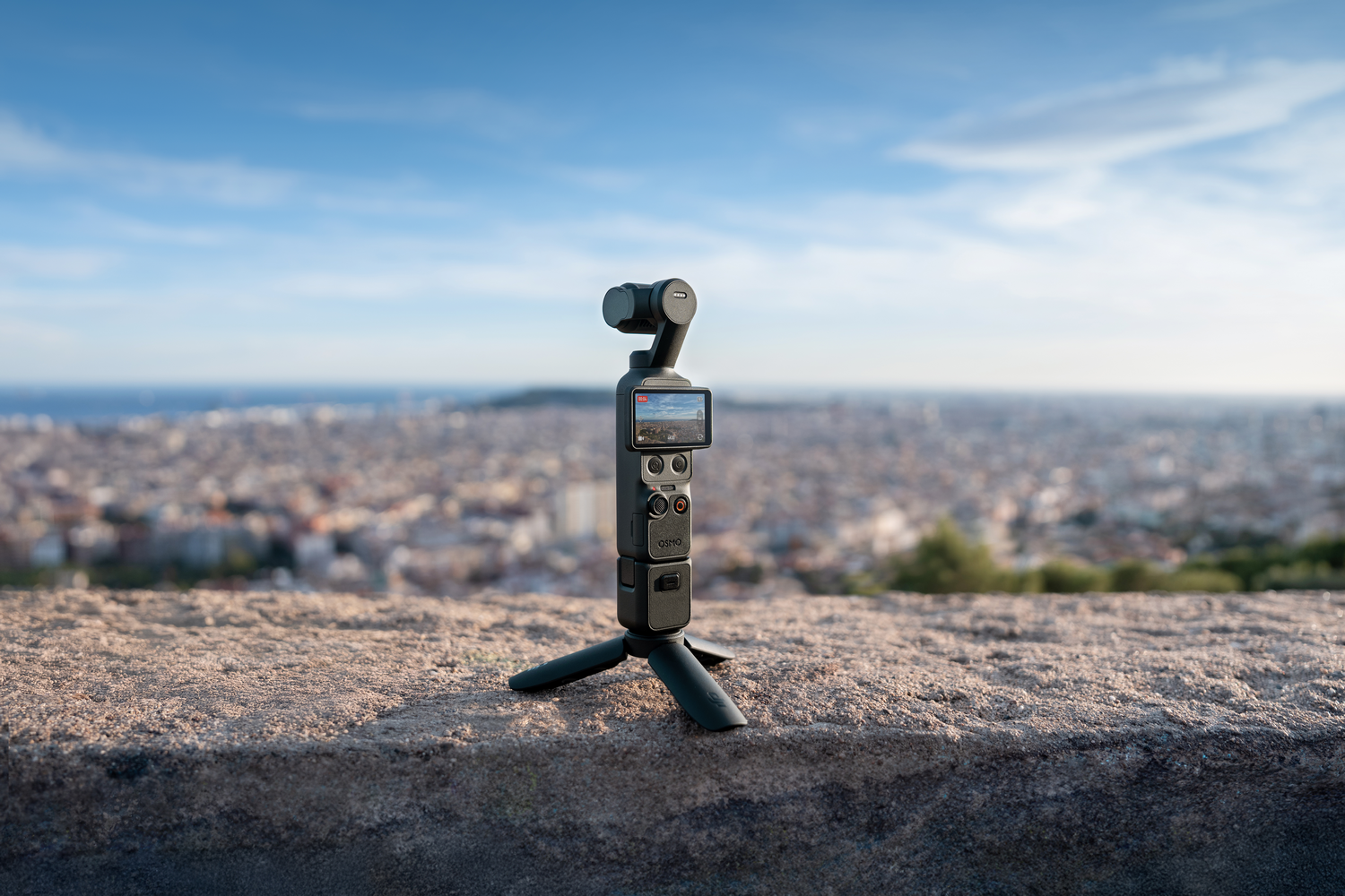 Un estabilizador cardán negro está sobre un trípode en una piedra con una ciudad al fondo.