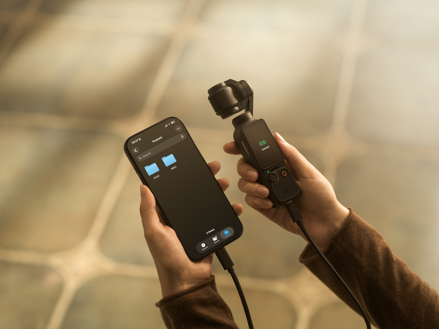 Manos sostienen un smartphone y un estabilizador de cardán conectados por cable.
