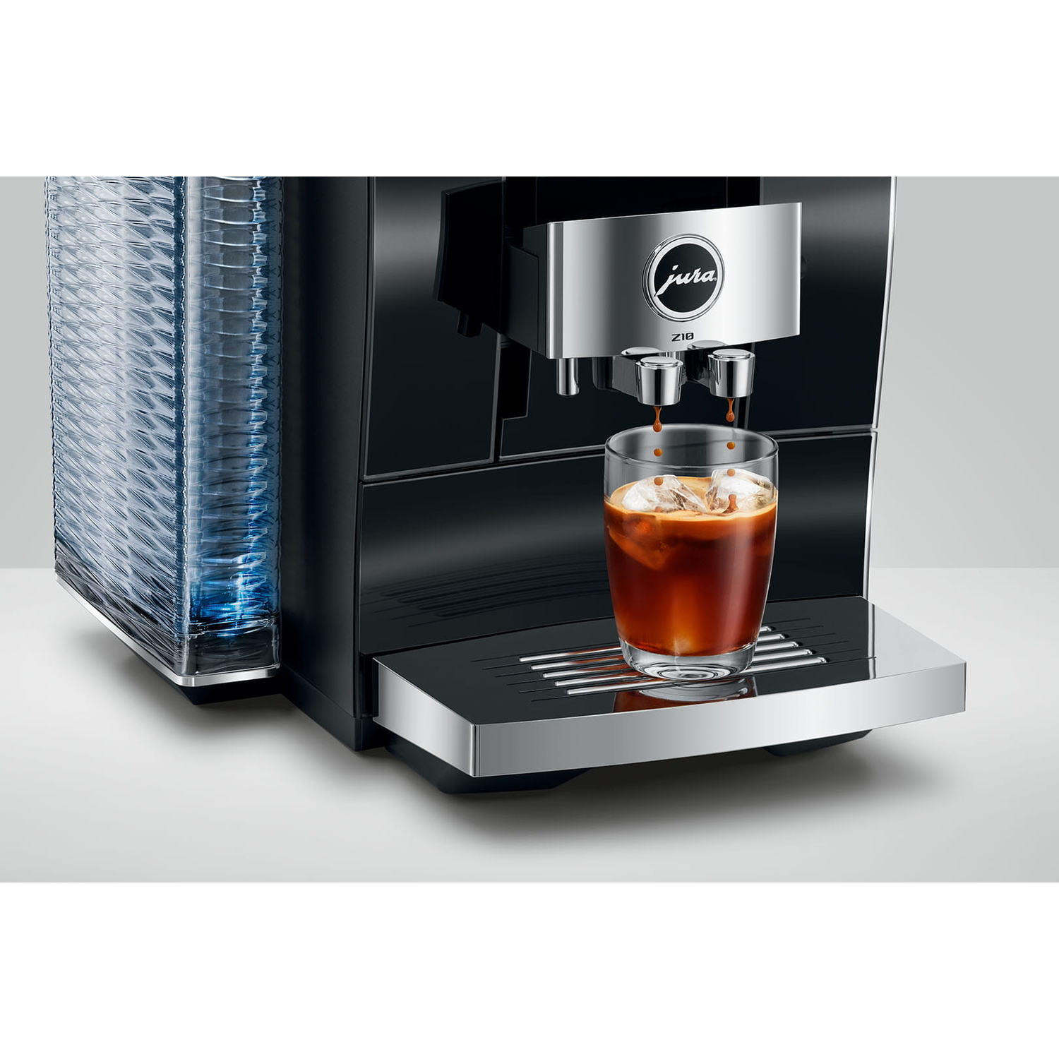 Een zwarte Jura Z10 koffiemachine die koffie in een glas met ijs schenkt, naast een stapel doorzichtige plastic bekers.