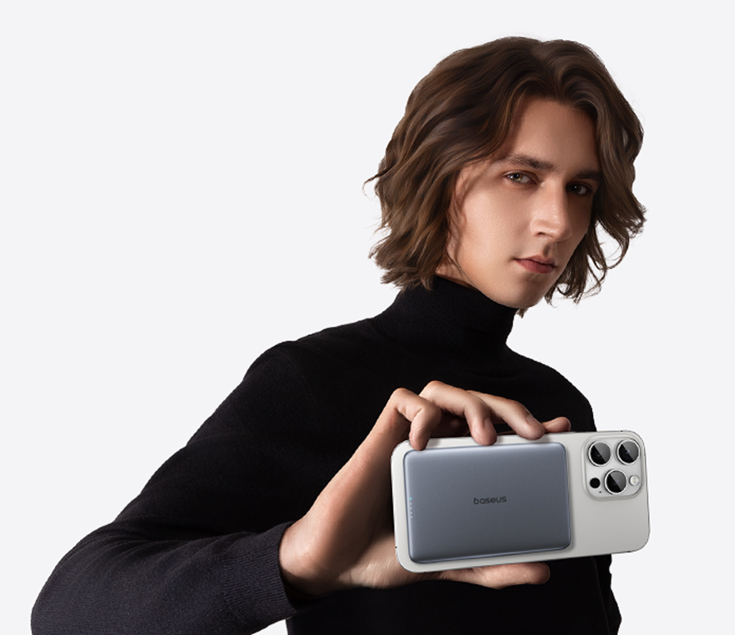 Hombre con jersey negro de cuello alto sostiene un teléfono blanco con power bank gris.