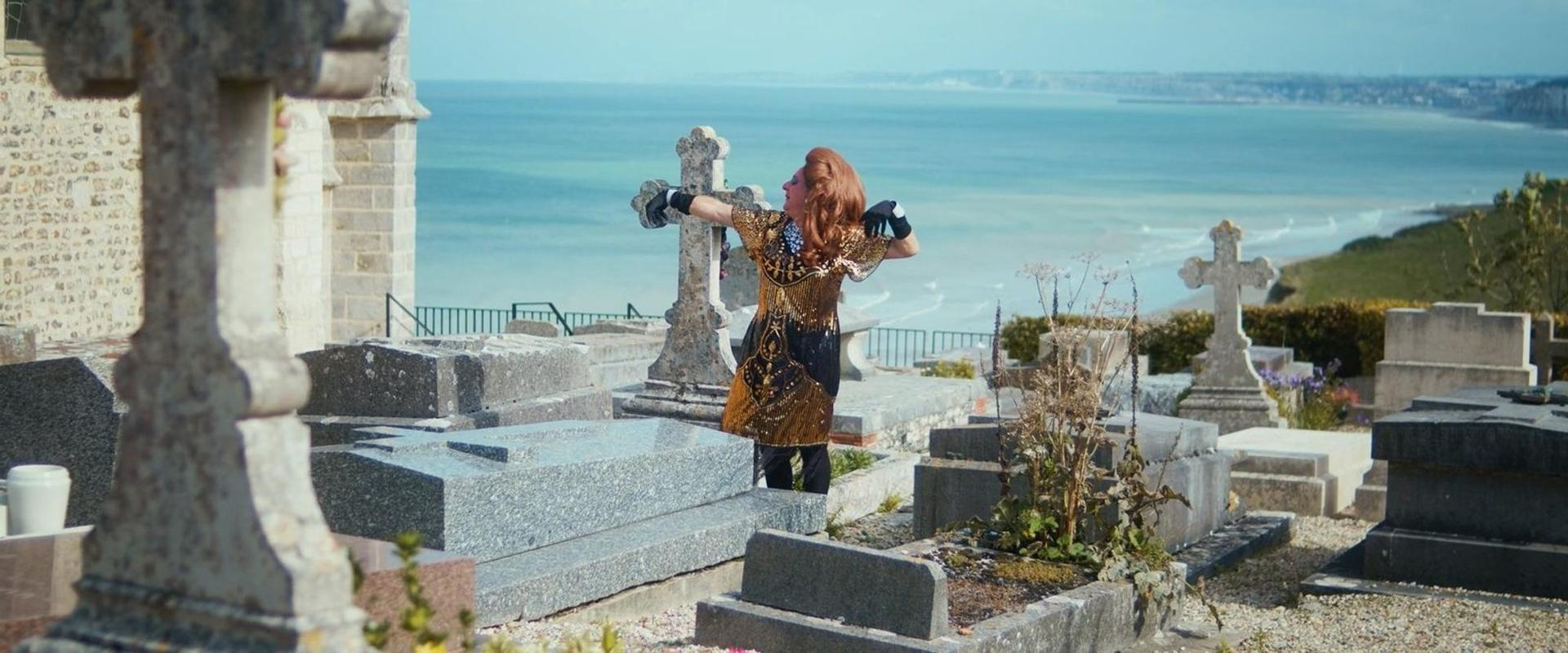 Eine Frau mit roten Haaren steht auf einem Friedhof am Meer.