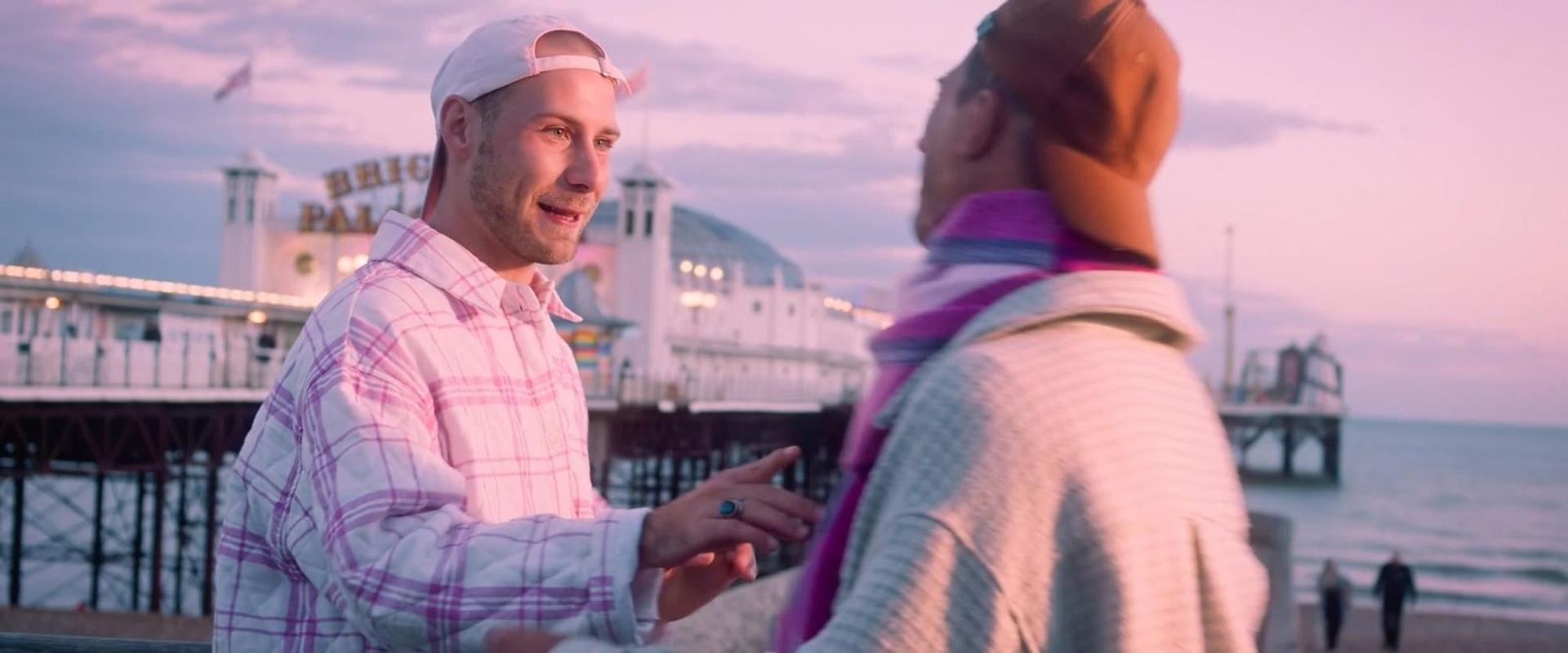 Zwei Männer unterhalten sich am Strand bei Sonnenuntergang vor einem Pier.