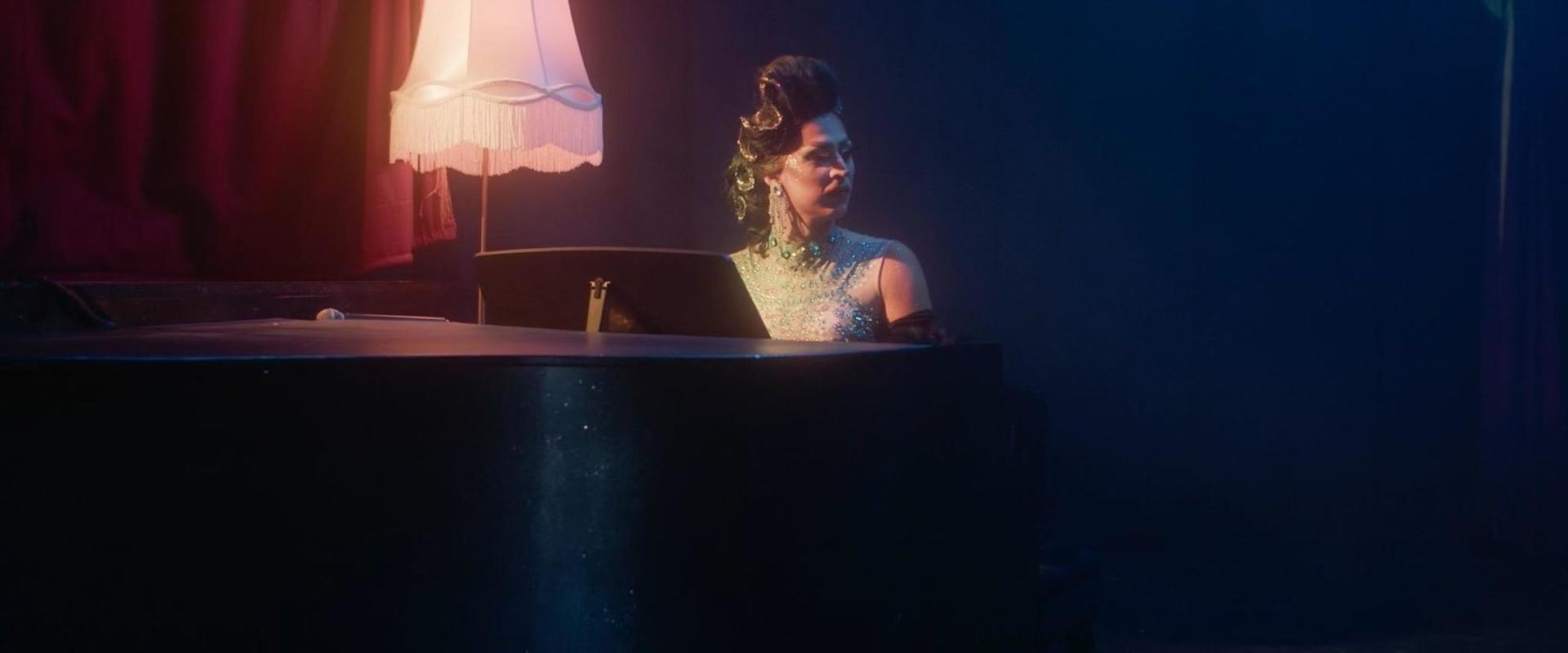 Eine Frau in einem glitzernden Kleid sitzt hinter einem Klavier.