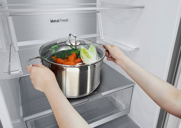 Osoba stawia garnek z warzywami na szufladzie w lodówce.
