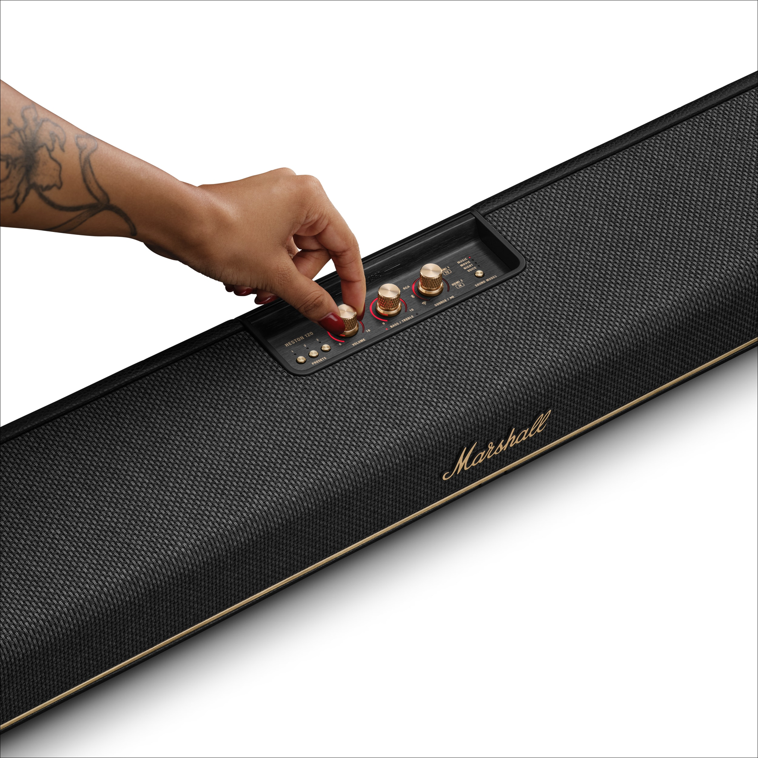 Een getatoeëerde hand stelt een gouden knop af op een zwarte Marshall soundbar.