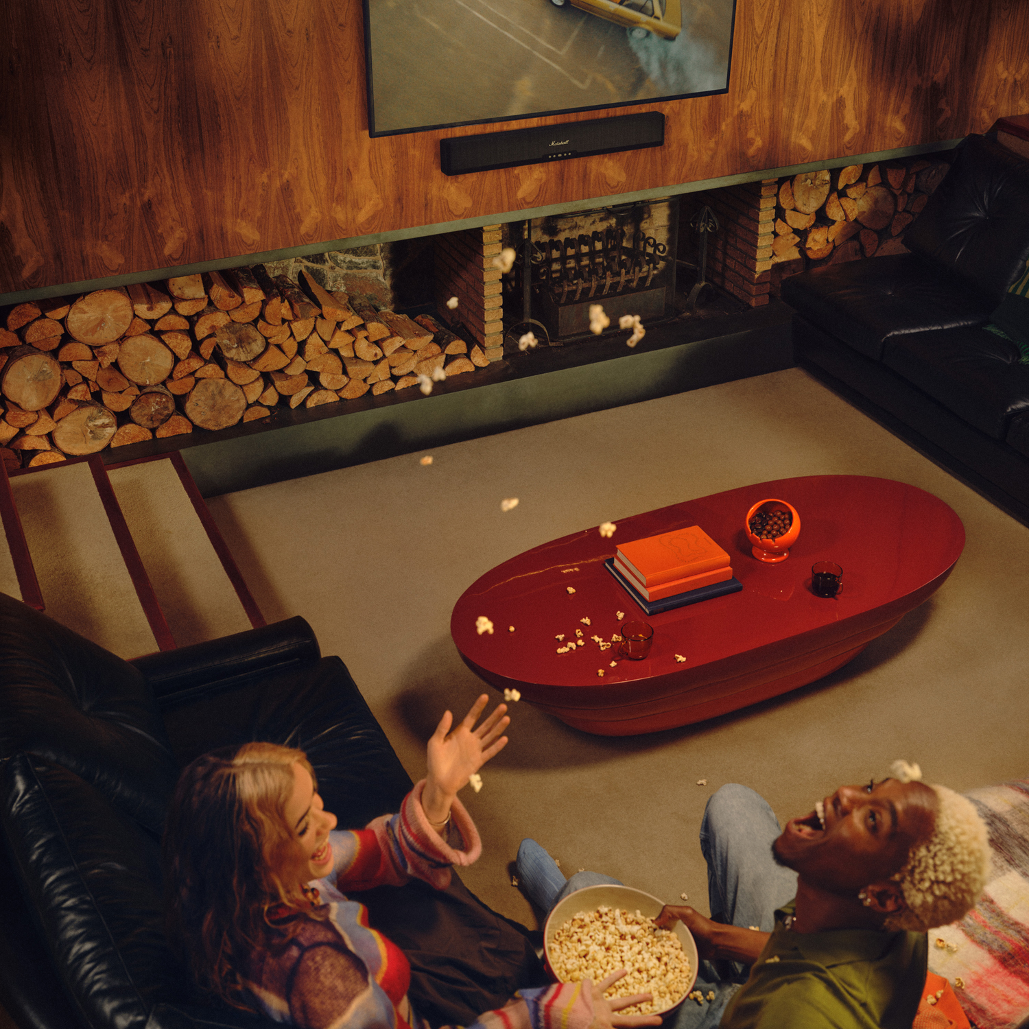 Twee lachende mensen met popcorn genieten van een film voor een open haard.