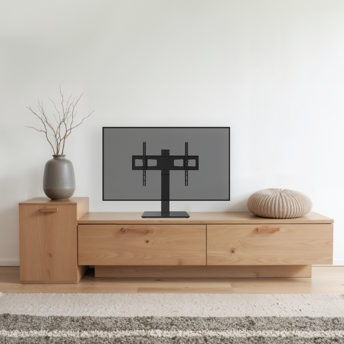 Une télévision est posée sur un meuble en bois. Un vase avec des branches est à gauche.