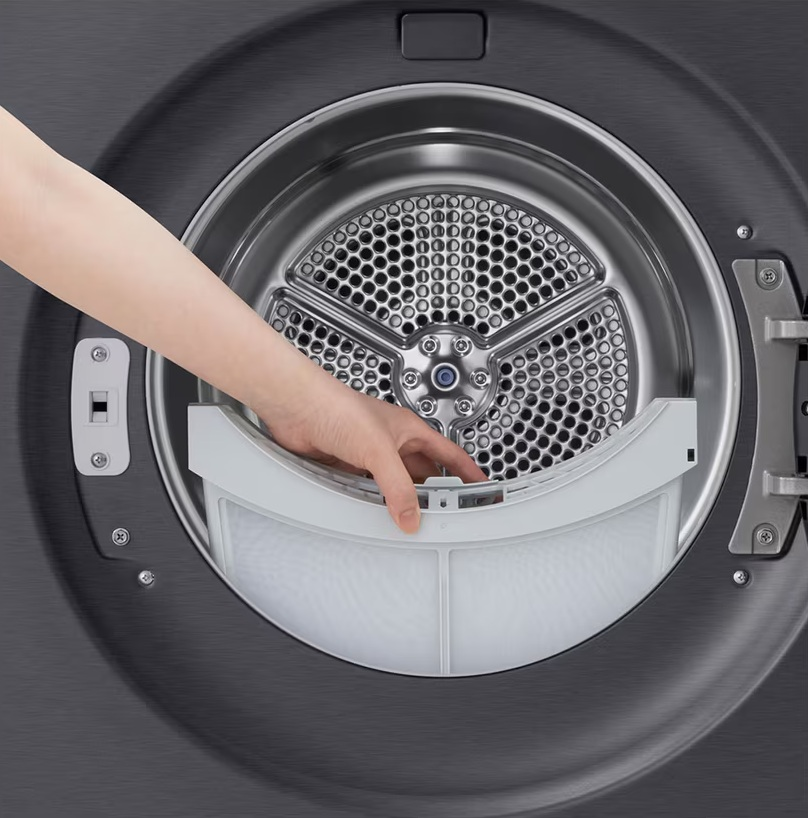 Ręka wyjmuje biały filtr kłaczków z bębna suszarki.
