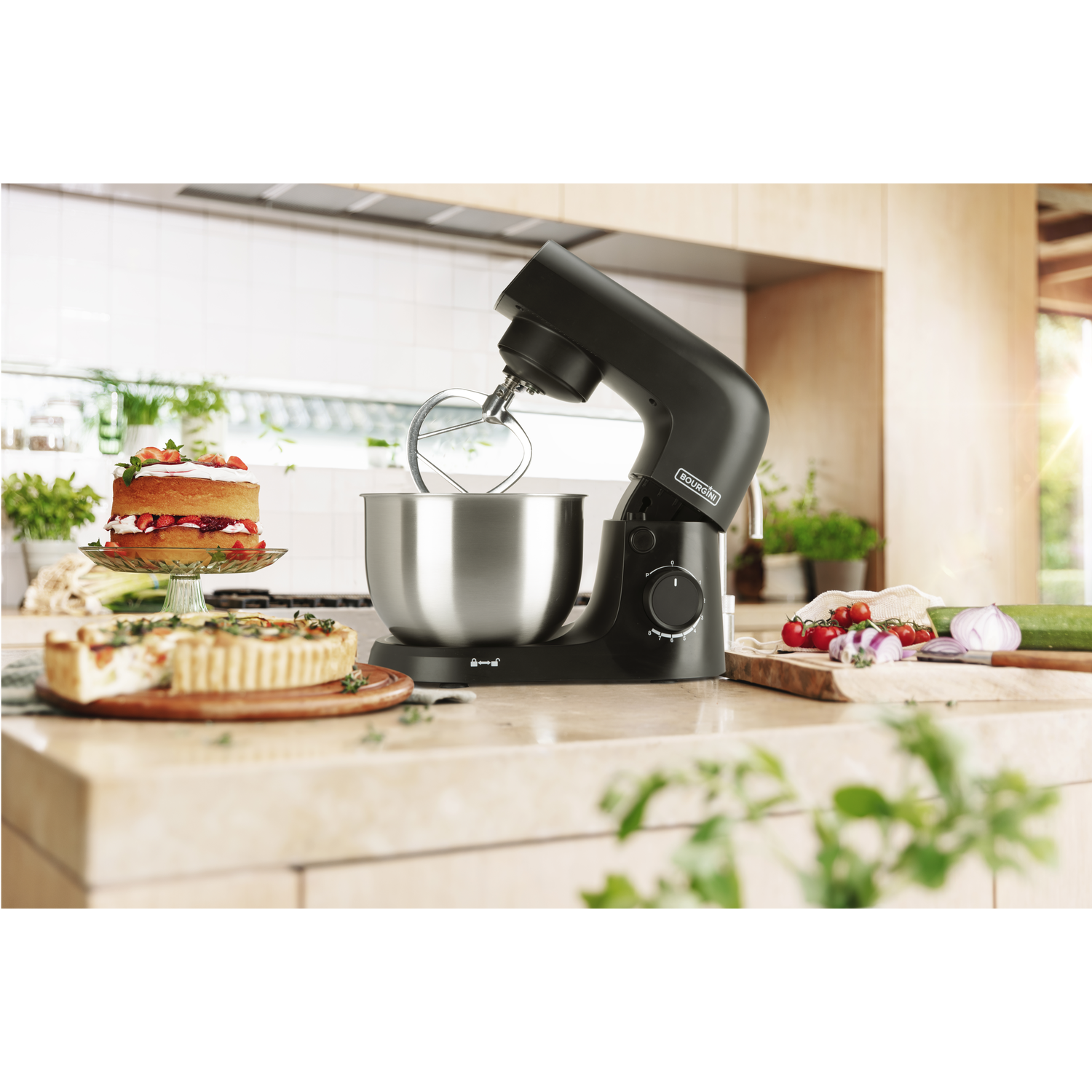 A black kitchen mixer with a bowl, beside it a cake and a savory tart.