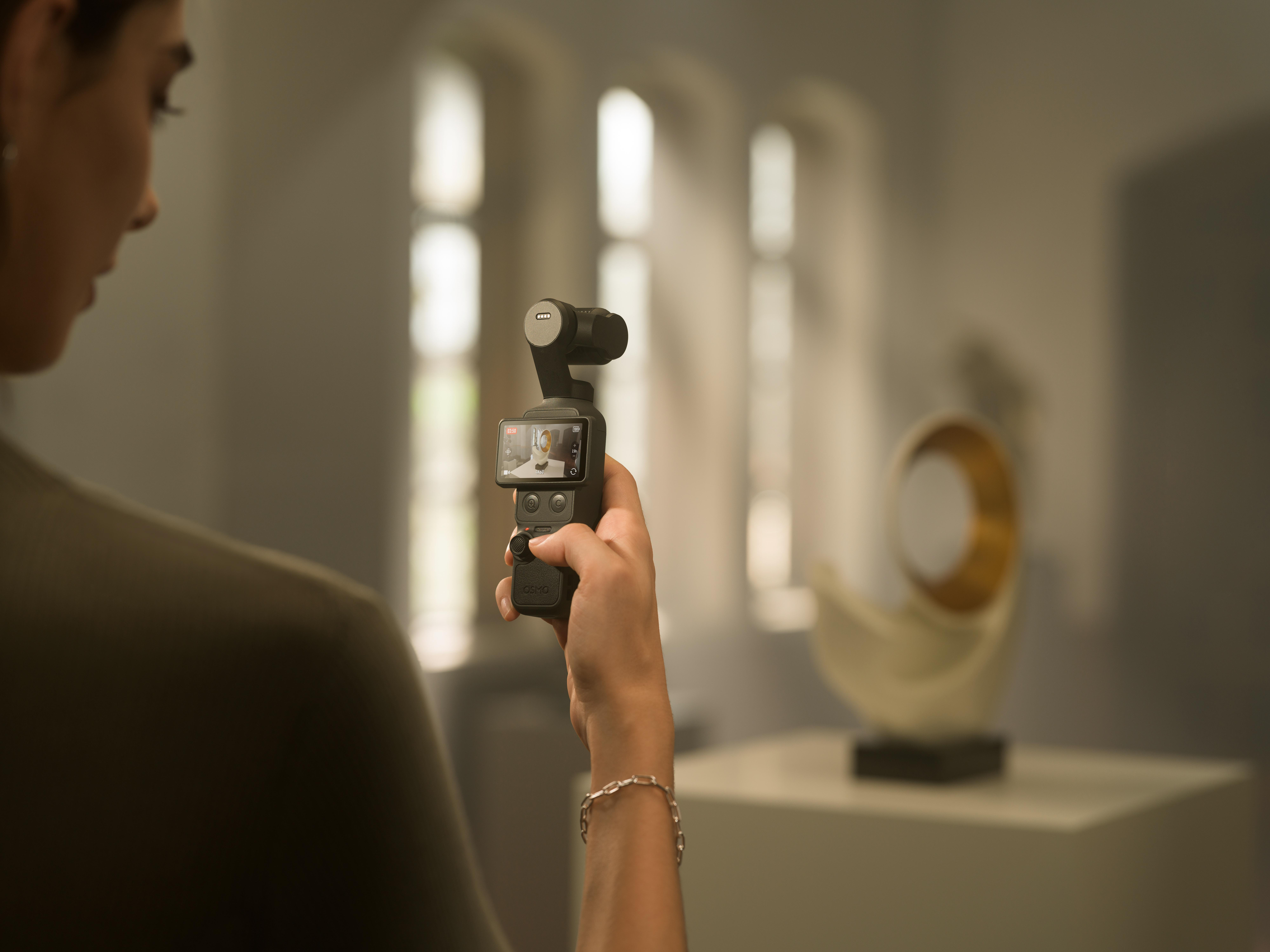 Eine Hand hält eine Kamera mit Bildschirm in einem hellen Raum mit Fenstern.